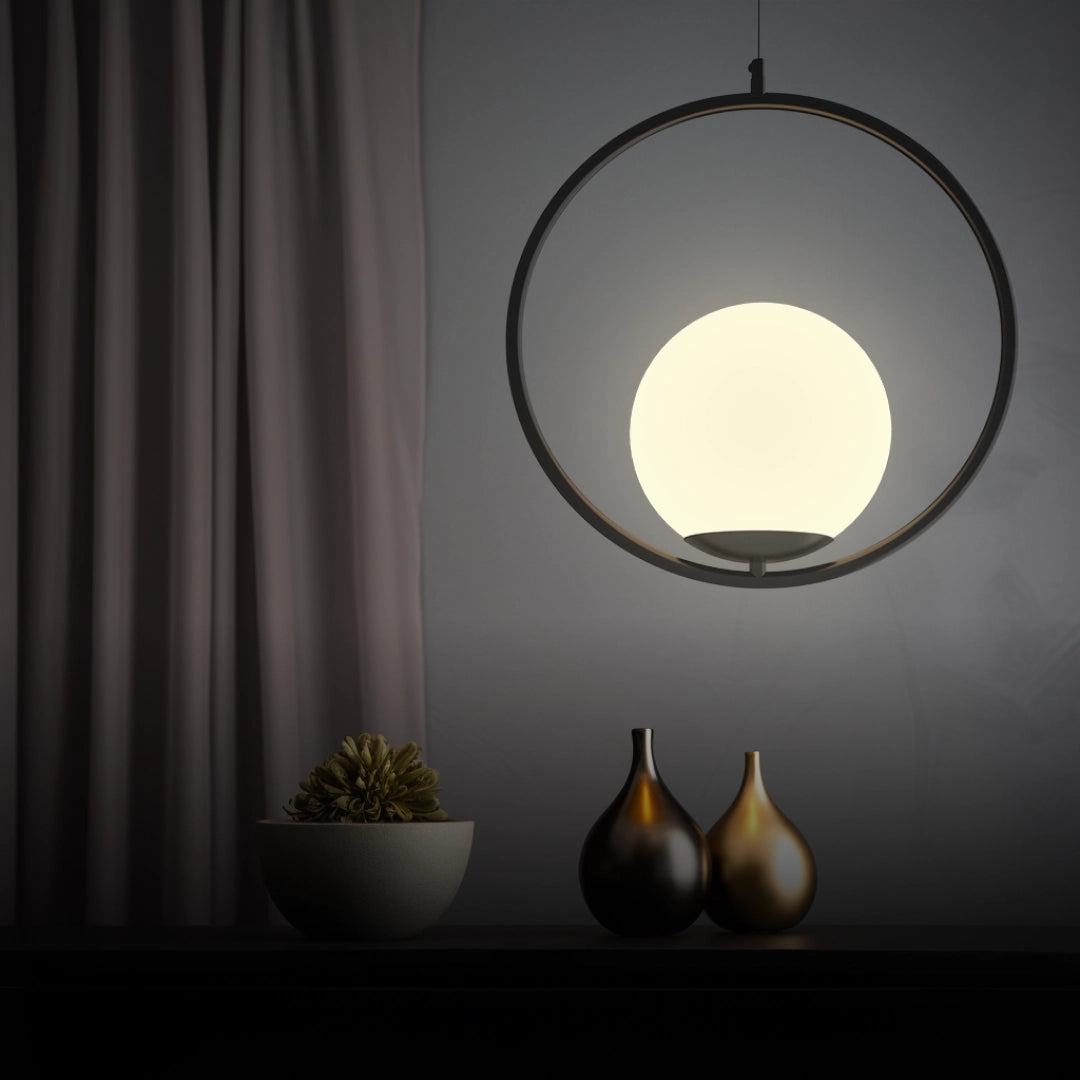 Modern LED round bedside lamp in black, emitting cold white light, displayed on a wooden surface with decorative plant elements and a neutral interior backdrop featuring a curtain.