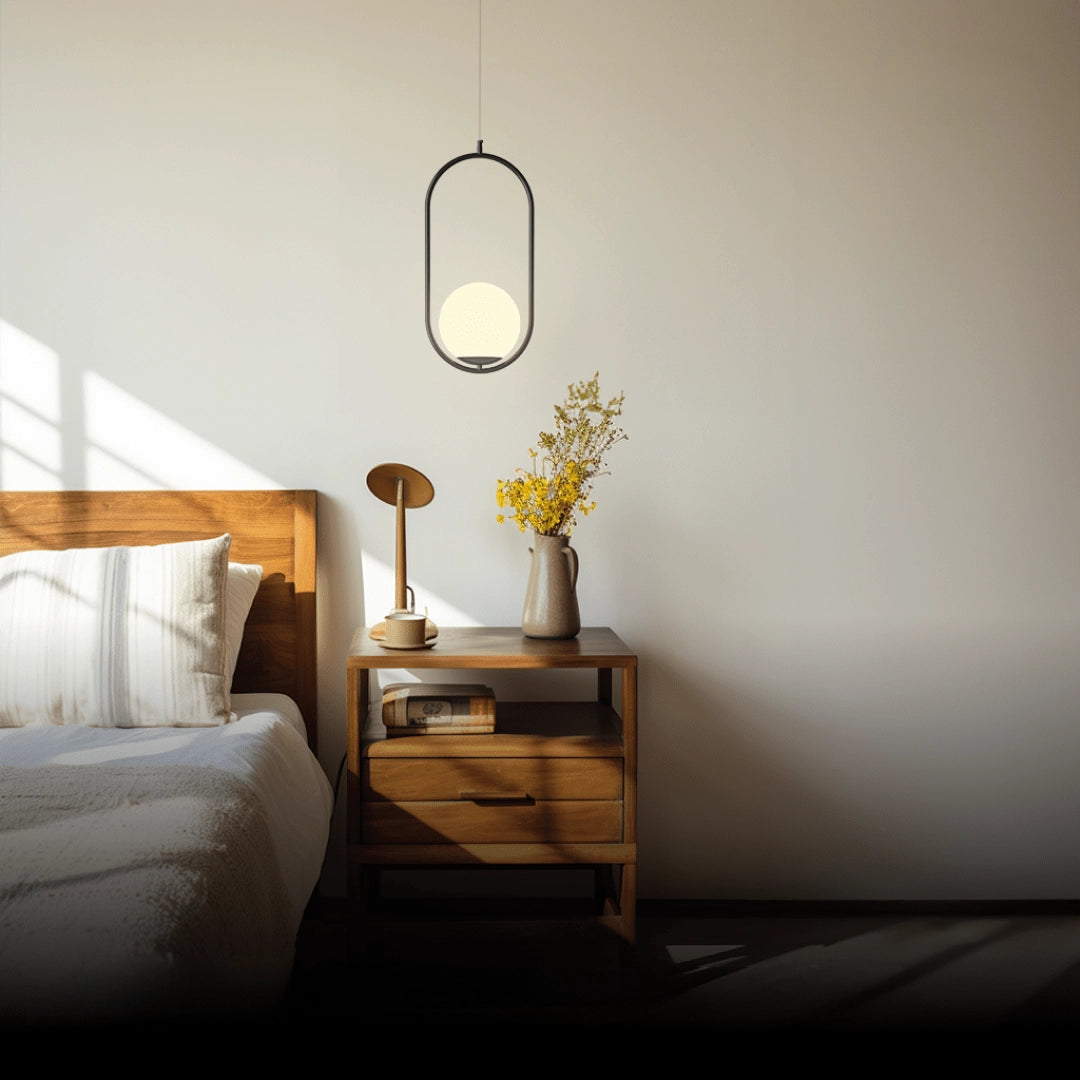 Modern LED round bedside lamp in black finish with cold white light, placed on a wooden table. Surrounded by minimalistic interior decor elements, including a small houseplant for a cozy and stylish bedroom setting.