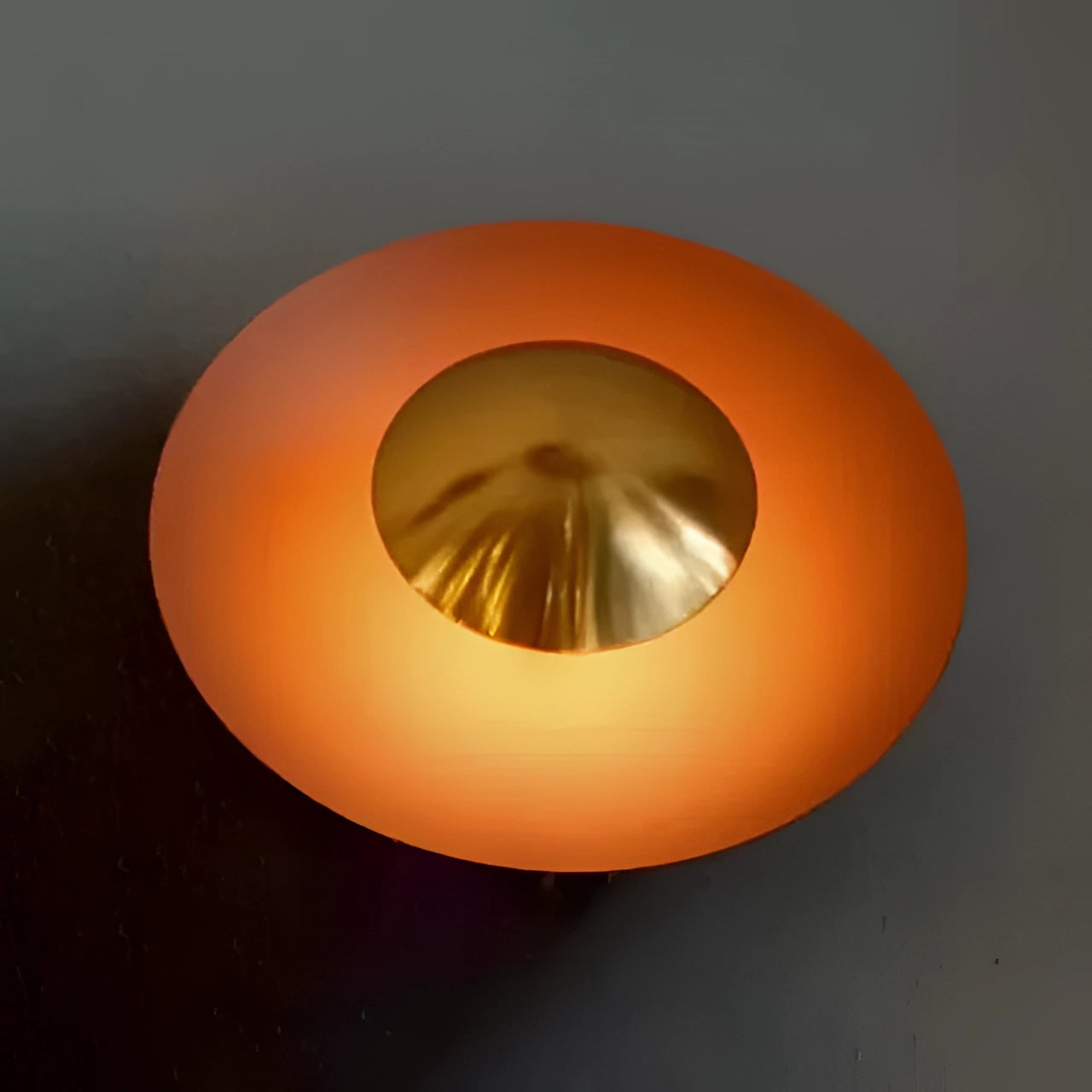 Modern LED wall lamp in a minimalistic design featuring a brass decorative sconce, showcased in an orange shade with gold accents. The lamp is 60cm in length and emits a cold white light. The image highlights the lamp's sleek and artistic attributes, emphasizing its circular shape and elegant appearance.