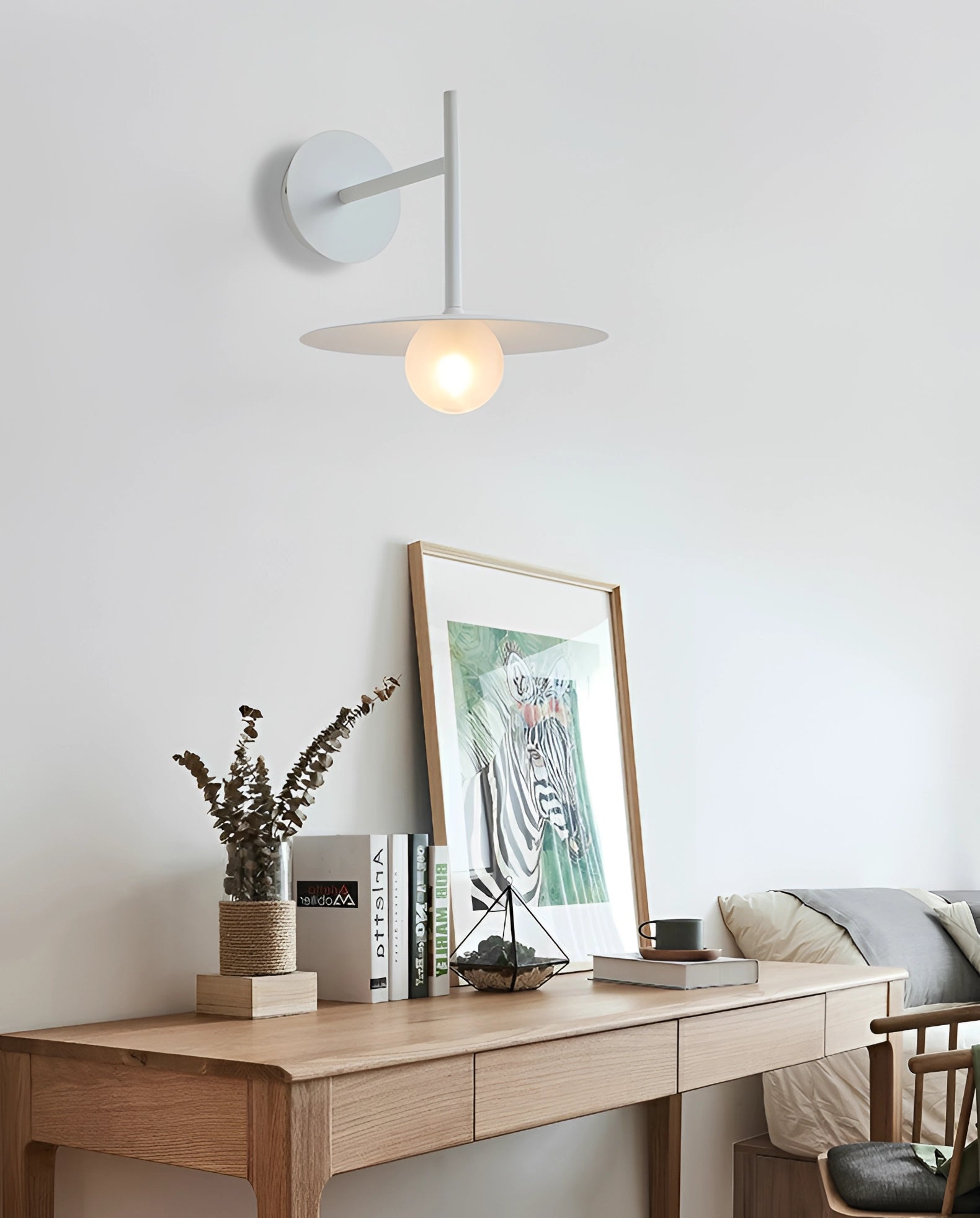 Modern matte black minimalist wall sconce mounted on a wooden wall above a small table with a plant and picture frame, illuminating a cozy bedroom or hallway setting.