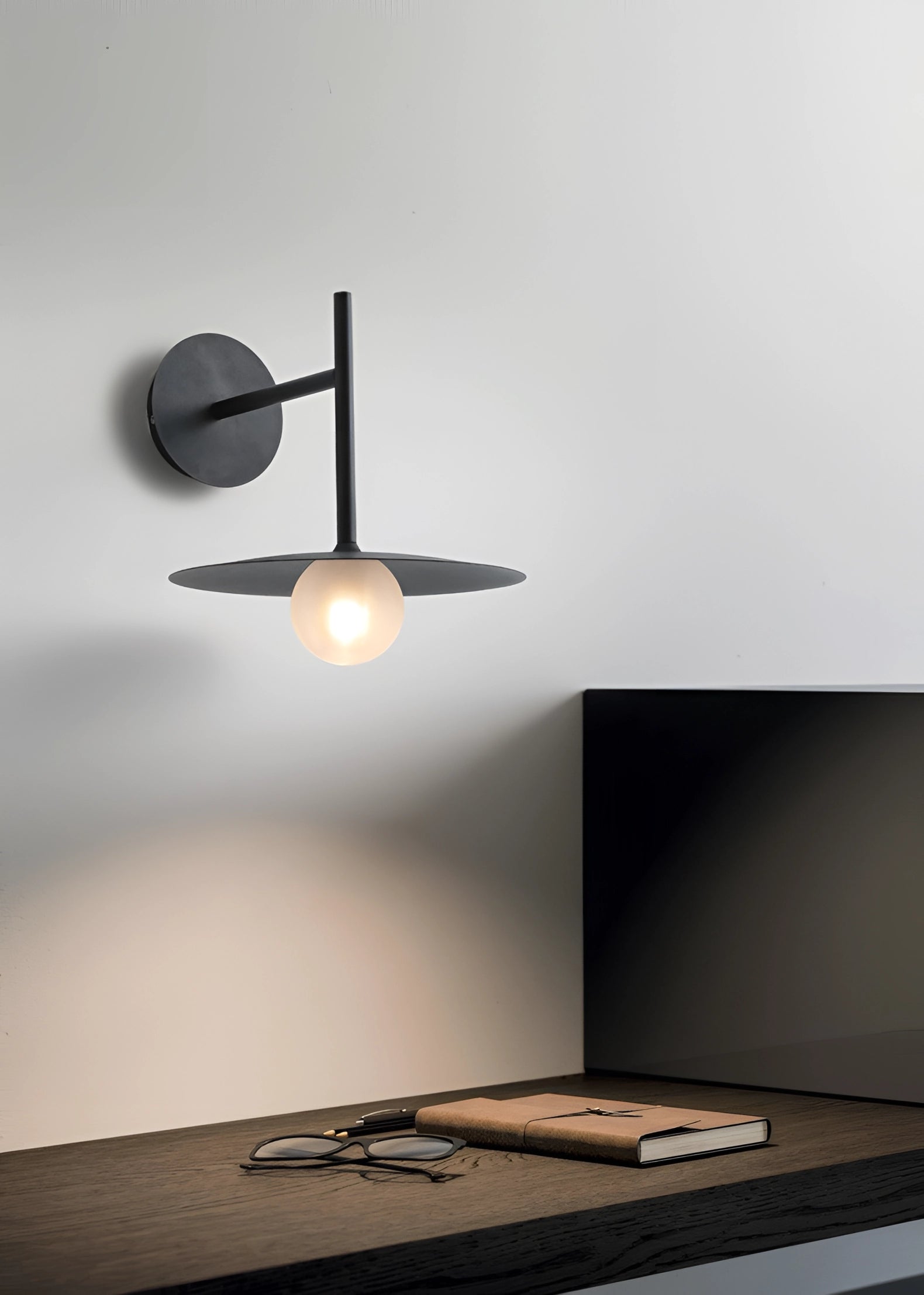 Modern matte black minimalist wall sconce mounted on a grey wall, featuring a sleek, contemporary design. Ideal for bedroom and hallway lighting, the sconce adds a sophisticated touch to interior decor with its clean lines and subtle tints and shades.