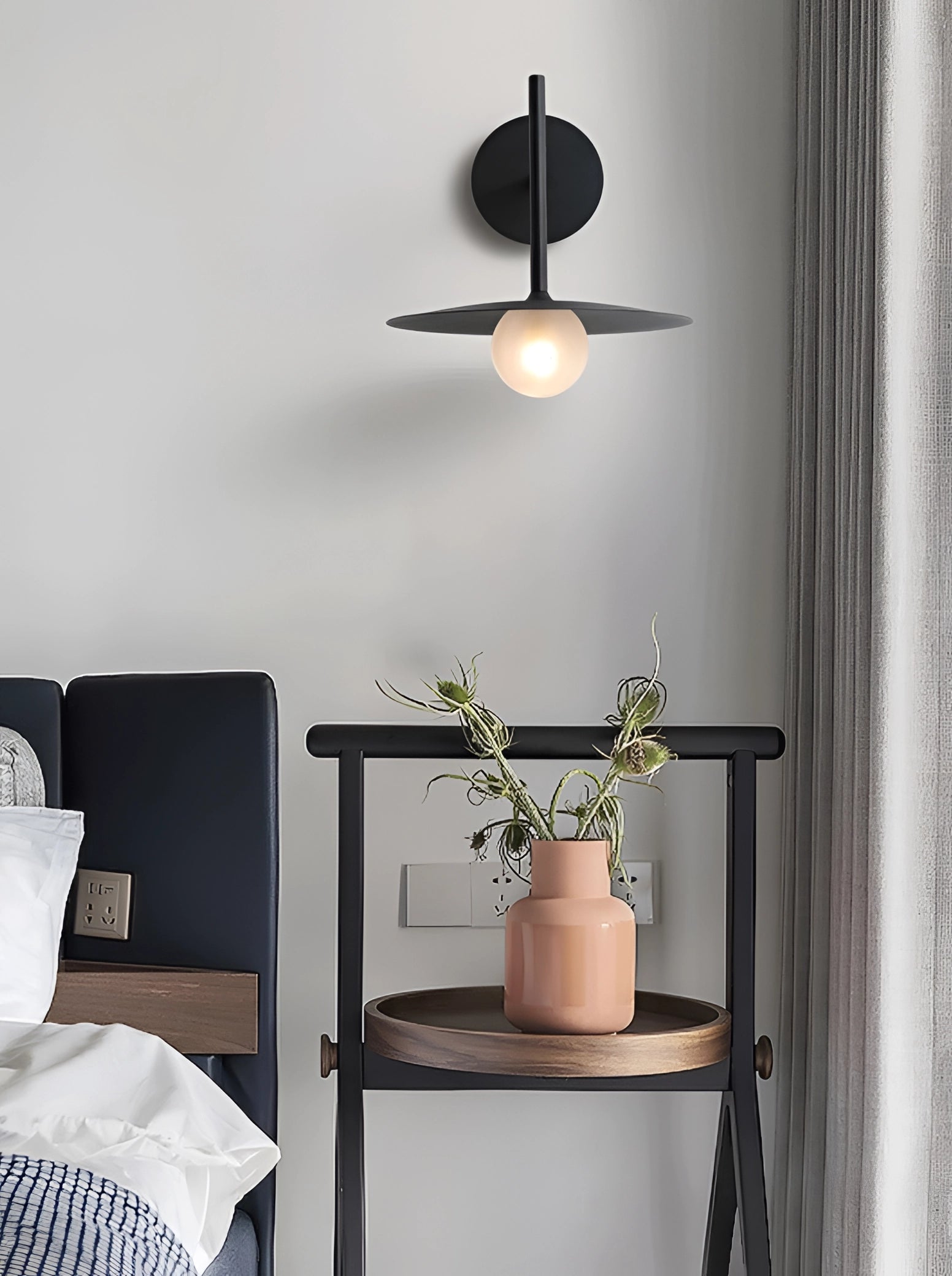 Modern matte black minimalist wall sconce mounted on a wall in a stylish interior setting, featuring a sleek design with warm ambient lighting.