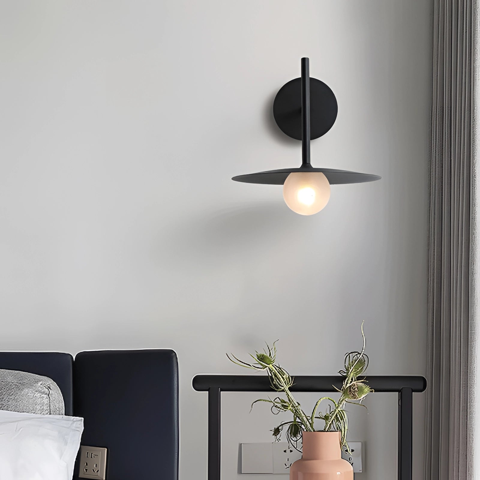 Modern matte black minimalist wall sconce mounted on a wall, illuminating a contemporary bedroom or hallway interior with sleek, understated elegance.