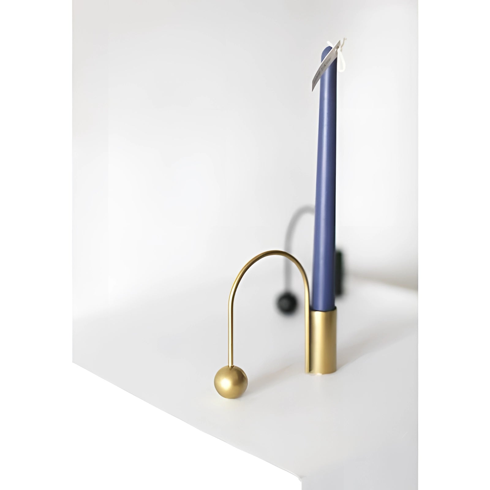 Modern minimalist brass candlestick featuring a unique, cylindrical design with a sleek metal finish, displayed on a wooden surface.