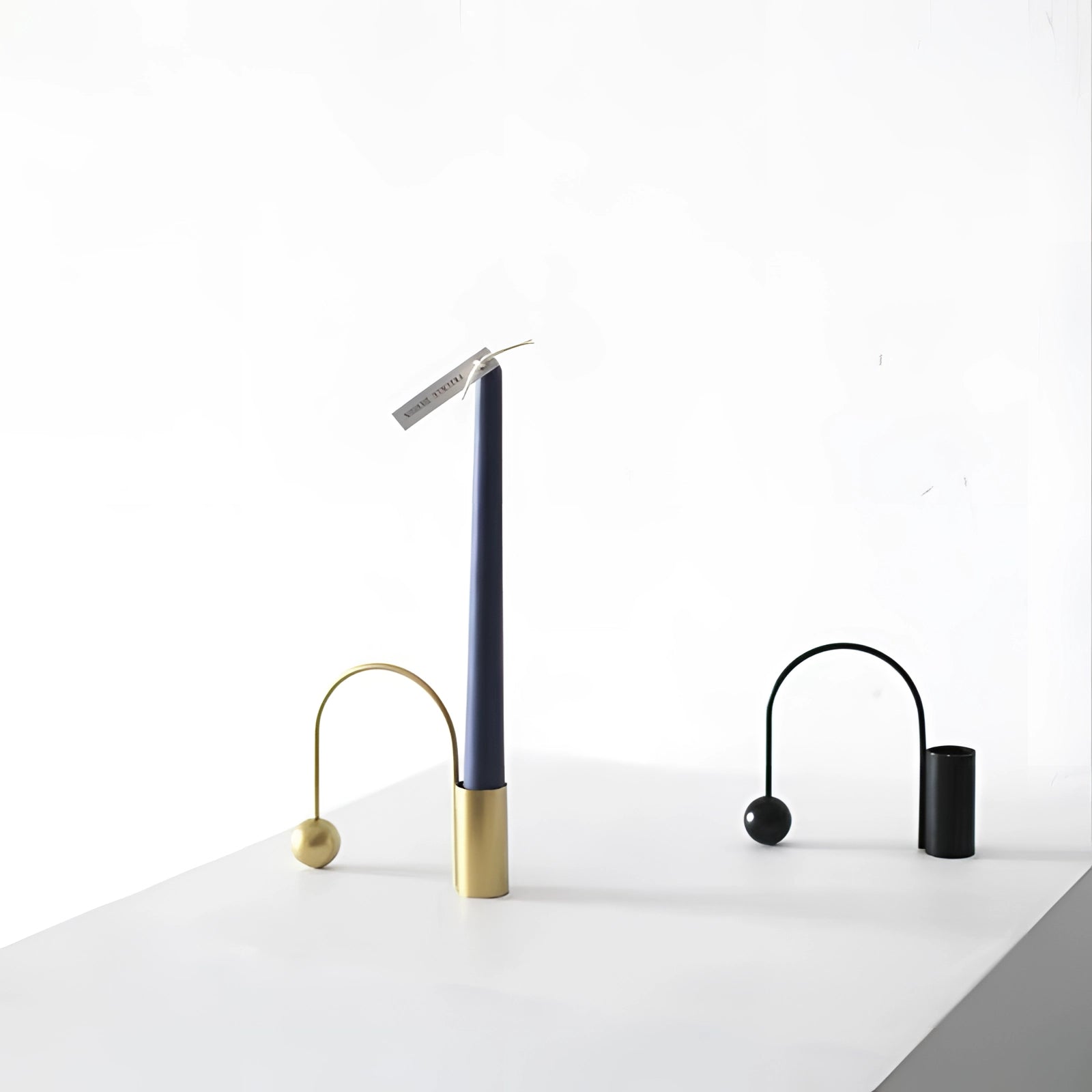 Modern minimalist brass candlestick with a sleek and unique design, featuring a rectangular and circular shape with a metallic finish, resting on a wooden surface.