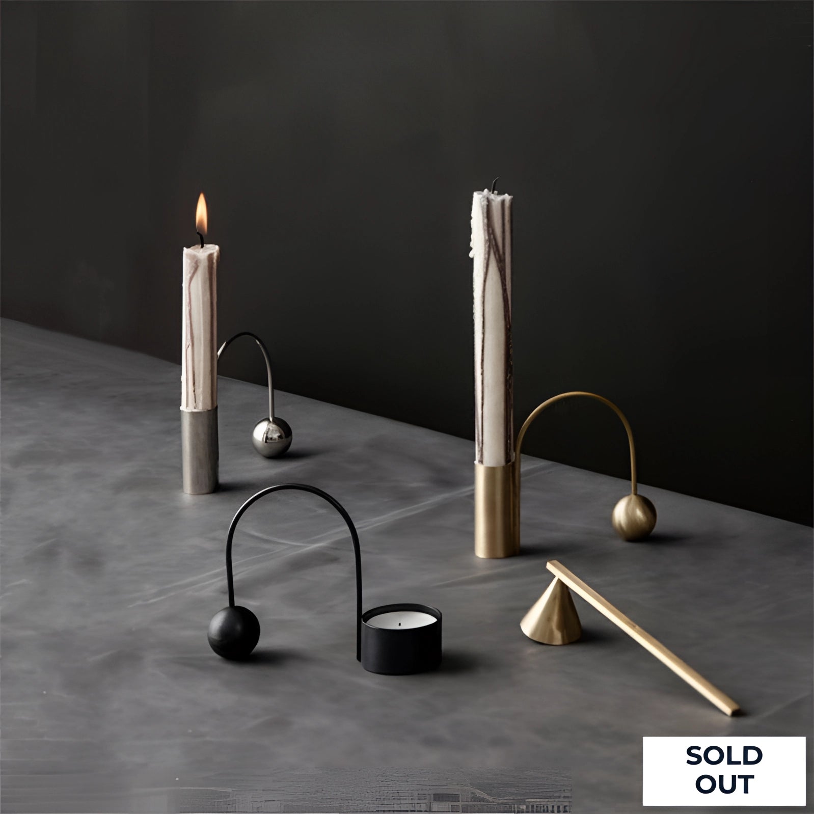 Modern minimalist brass candlestick with a unique designer shape, featuring a rectangular form and suitable for holding candles, shown on a wooden surface.