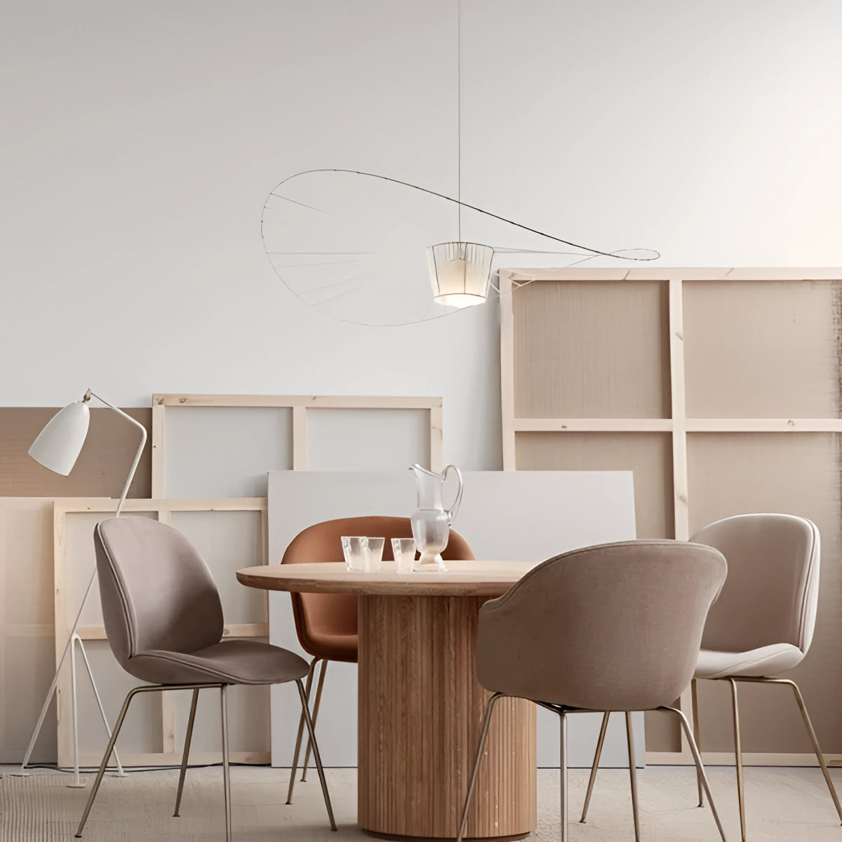 A modern minimalist ceiling fan with wing-shaped blades, featuring a sleek and contemporary design. The fan is installed in a modern interior setting with beige tones, surrounded by wooden furniture including a table and chairs, exemplifying stylish and functional architectural design.