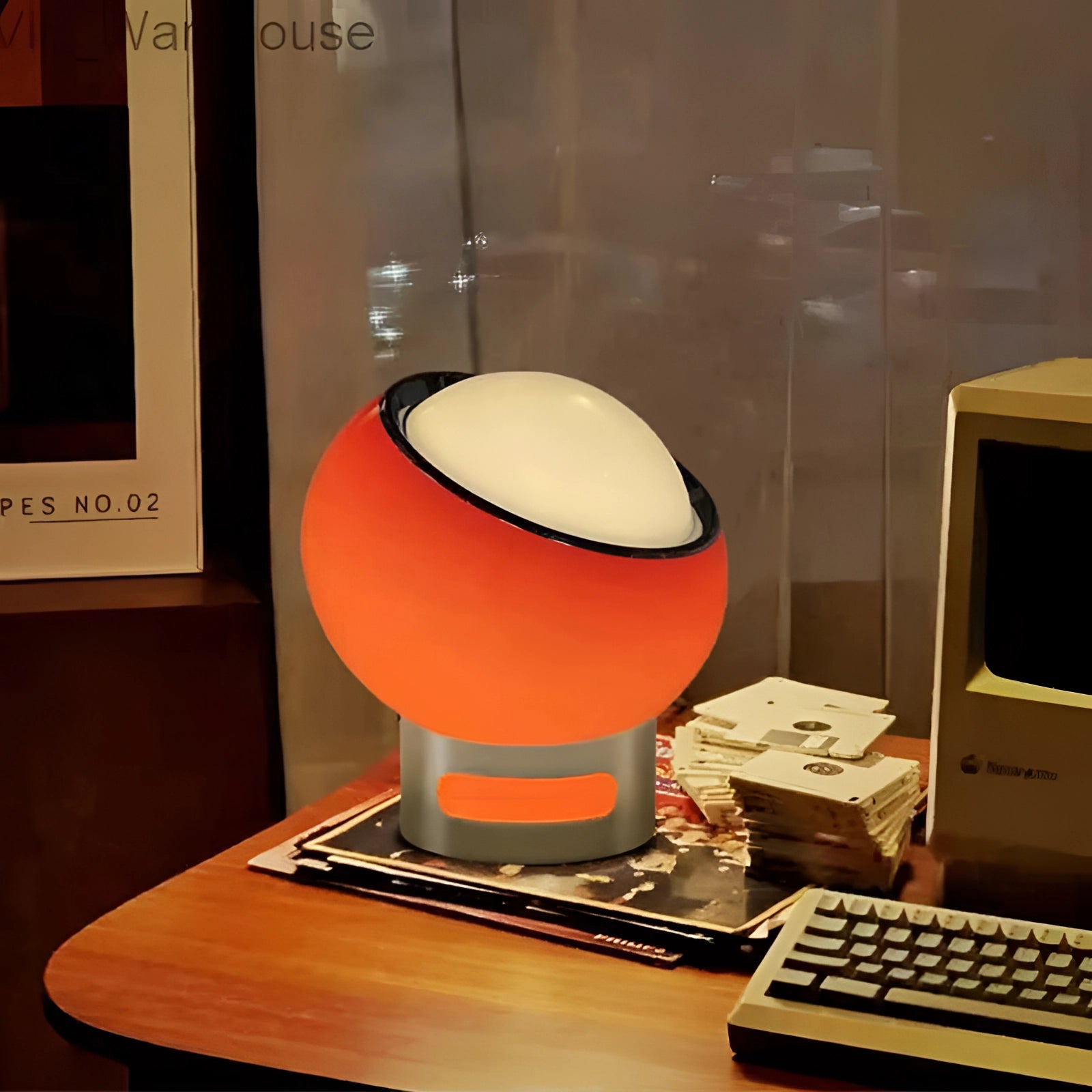 Modern minimalist circular LED bedside lamp with sleek metallic base on a desk, surrounded by computer peripherals, including a keyboard, monitor, and audio equipment.