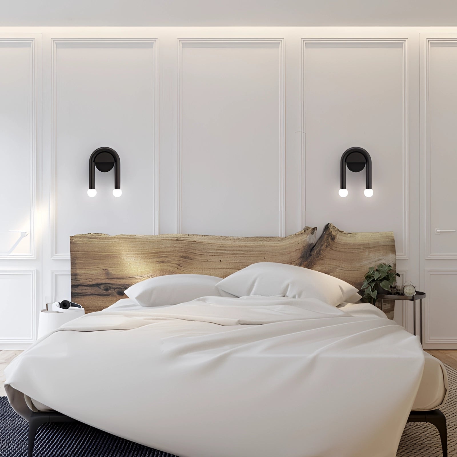 Modern minimalist LED dual wall lamp in black matte finish mounted on a white wall above wooden bed frame with white pillows in a contemporary interior design setting.