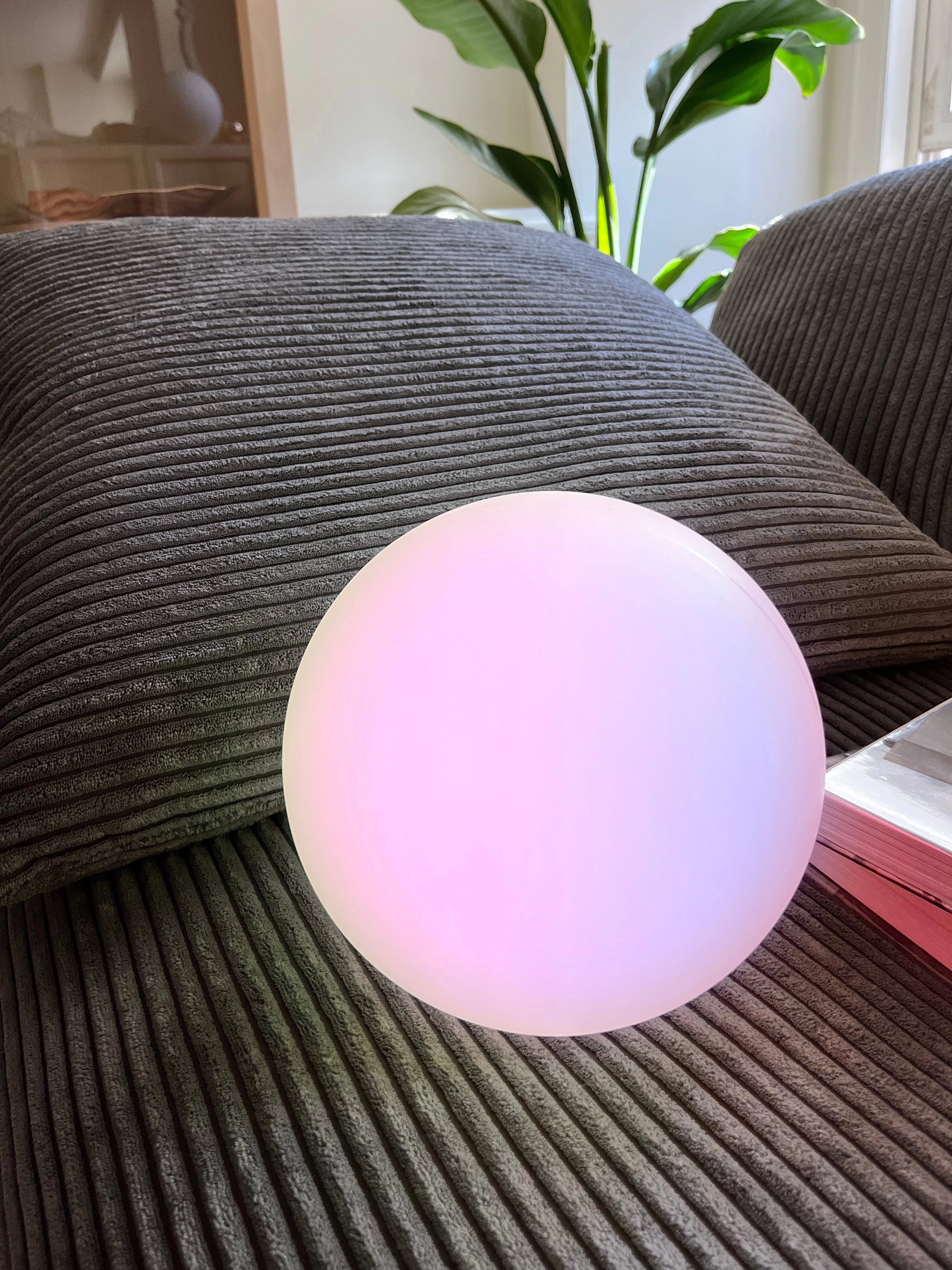 Modern Minimalist LED Globe Lamp on a wooden table with a plant and tablecloth nearby, creating a comfortable and stylish bedside setting.