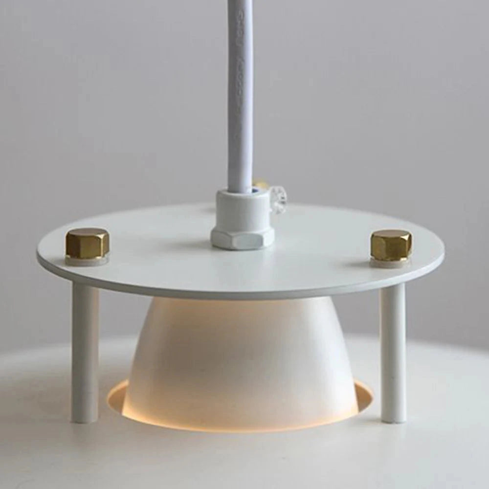 A modern minimalist LED pendant light with a Scandinavian design in white, suspended above a wooden table with clean lines, featuring elements of metal and composite materials, in a bright and contemporary setting.