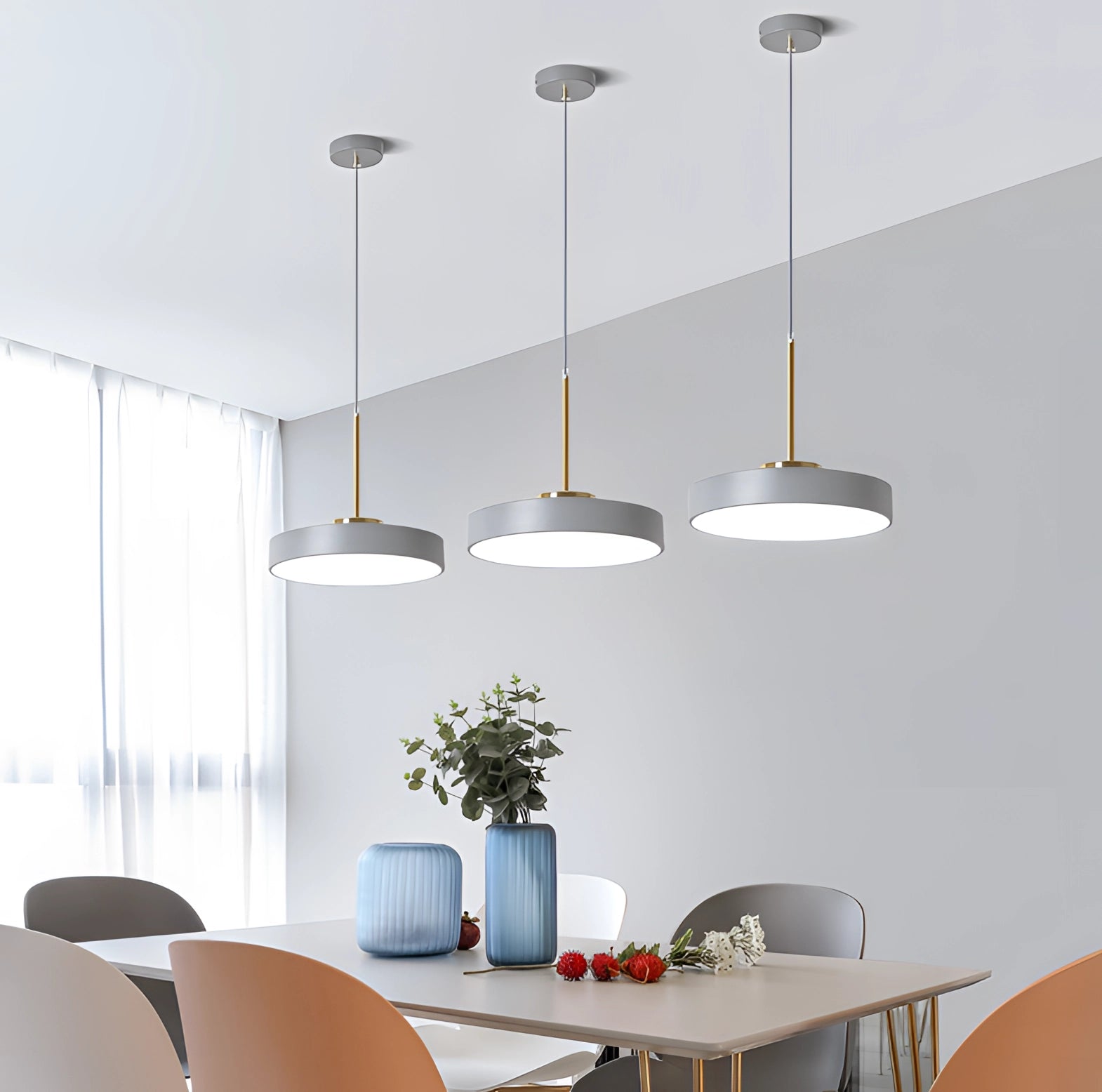 Modern minimalist LED pendant lights in gold and white hanging from the ceiling, illuminating a stylish room with a table, chairs, and a potted plant.
