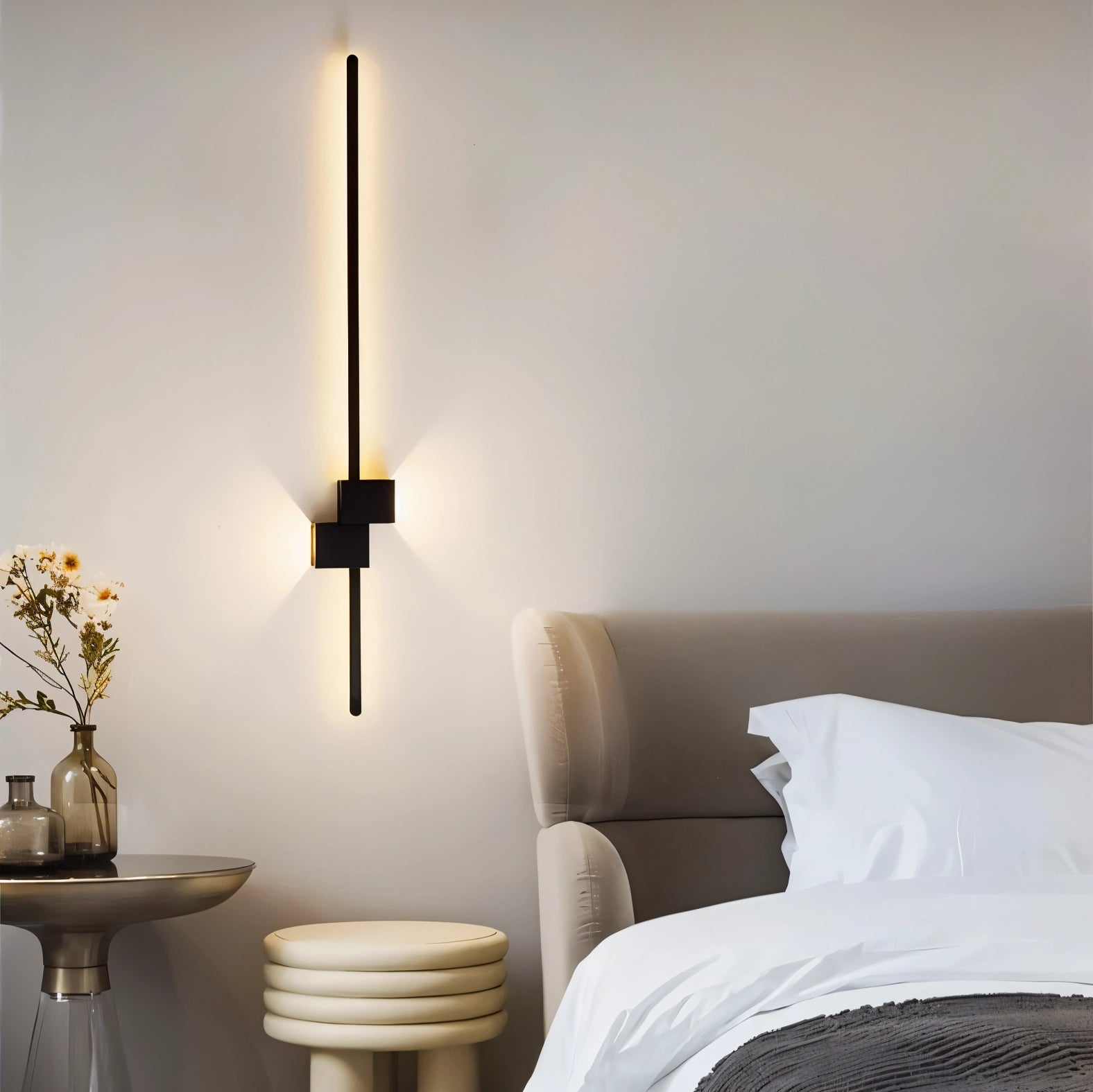Modern minimalist LED wall light mounted on a wall in a contemporary bedroom setting, surrounded by sleek furniture and decor, including a wooden side table, a potted houseplant, and a flowerpot, creating a comfortable and stylish interior design ambiance.