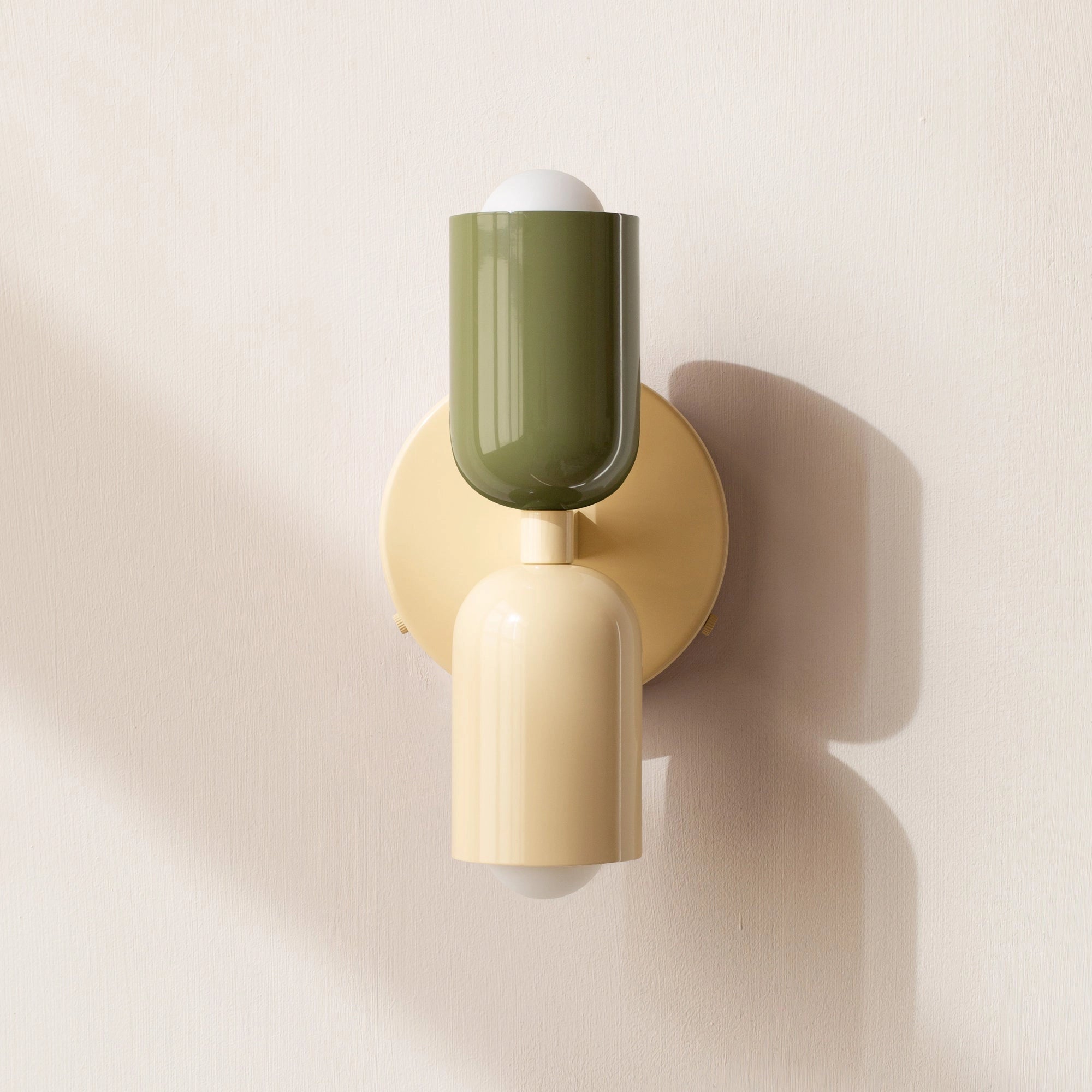 Modern minimalist LED wall sconce with a geometric dual head design, featuring a green, white, and beige color scheme, mounted on a wooden surface.