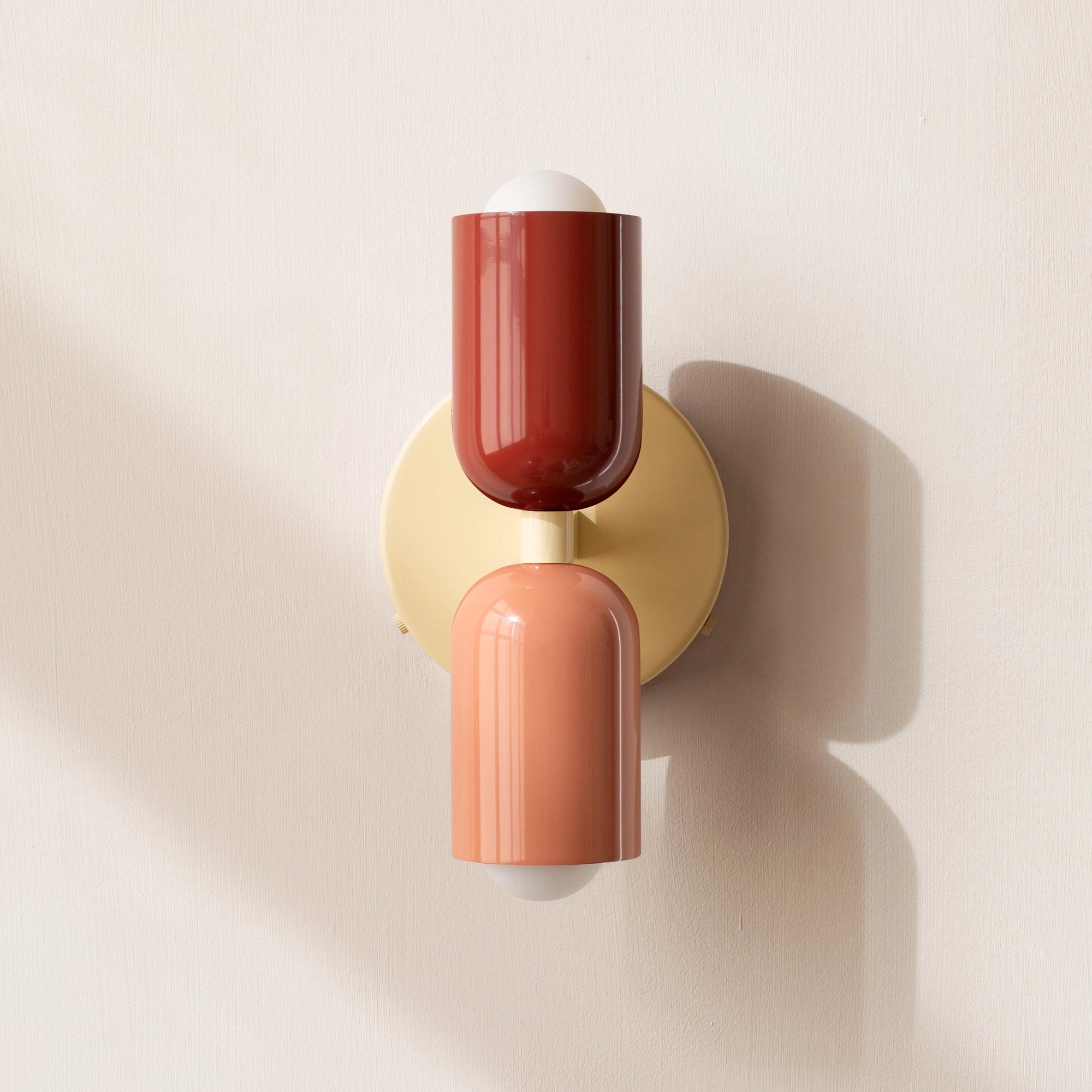 Modern minimalist LED wall sconce with a geometric dual head design in shades of red, salmon, and beige, featuring a sleek cylinder shape and contemporary aesthetic.