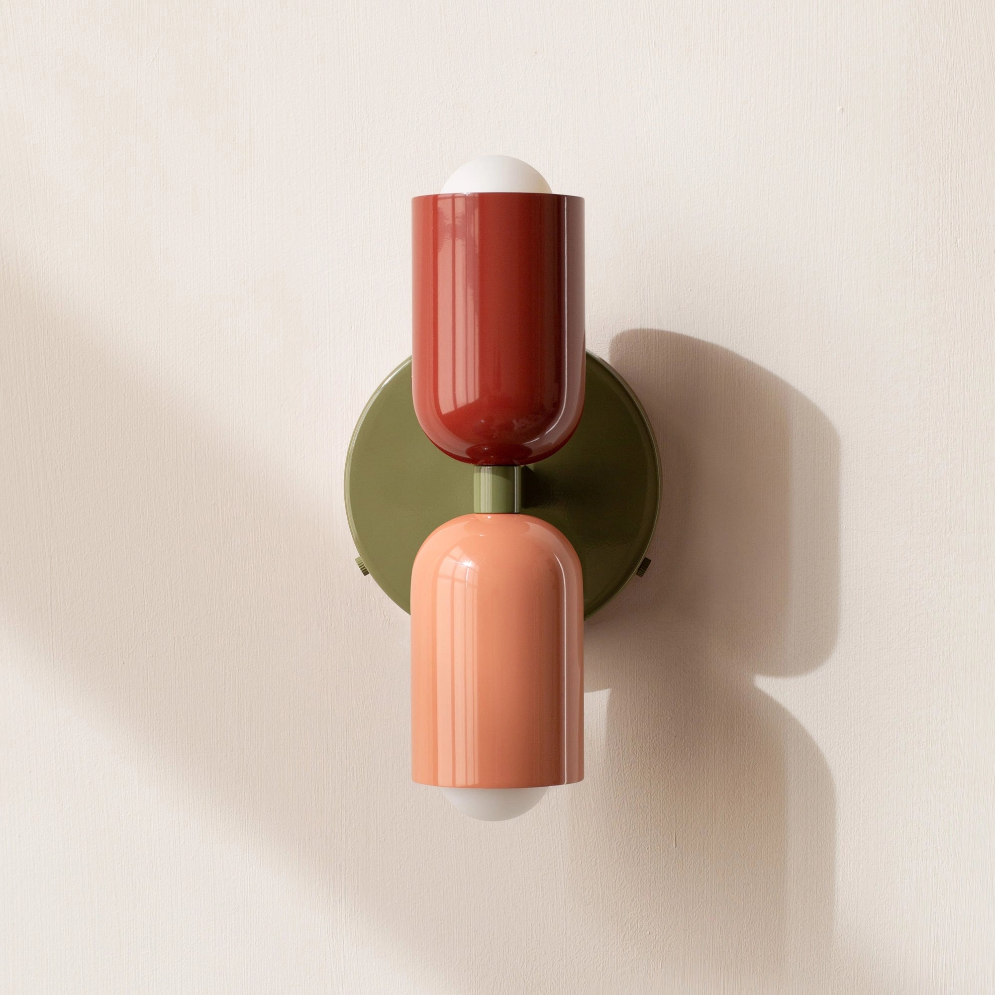 Modern minimalist LED wall sconce with a geometric dual head lamp design, featuring a mix of red, salmon, and green colors, set against a combination of wood and metal elements.