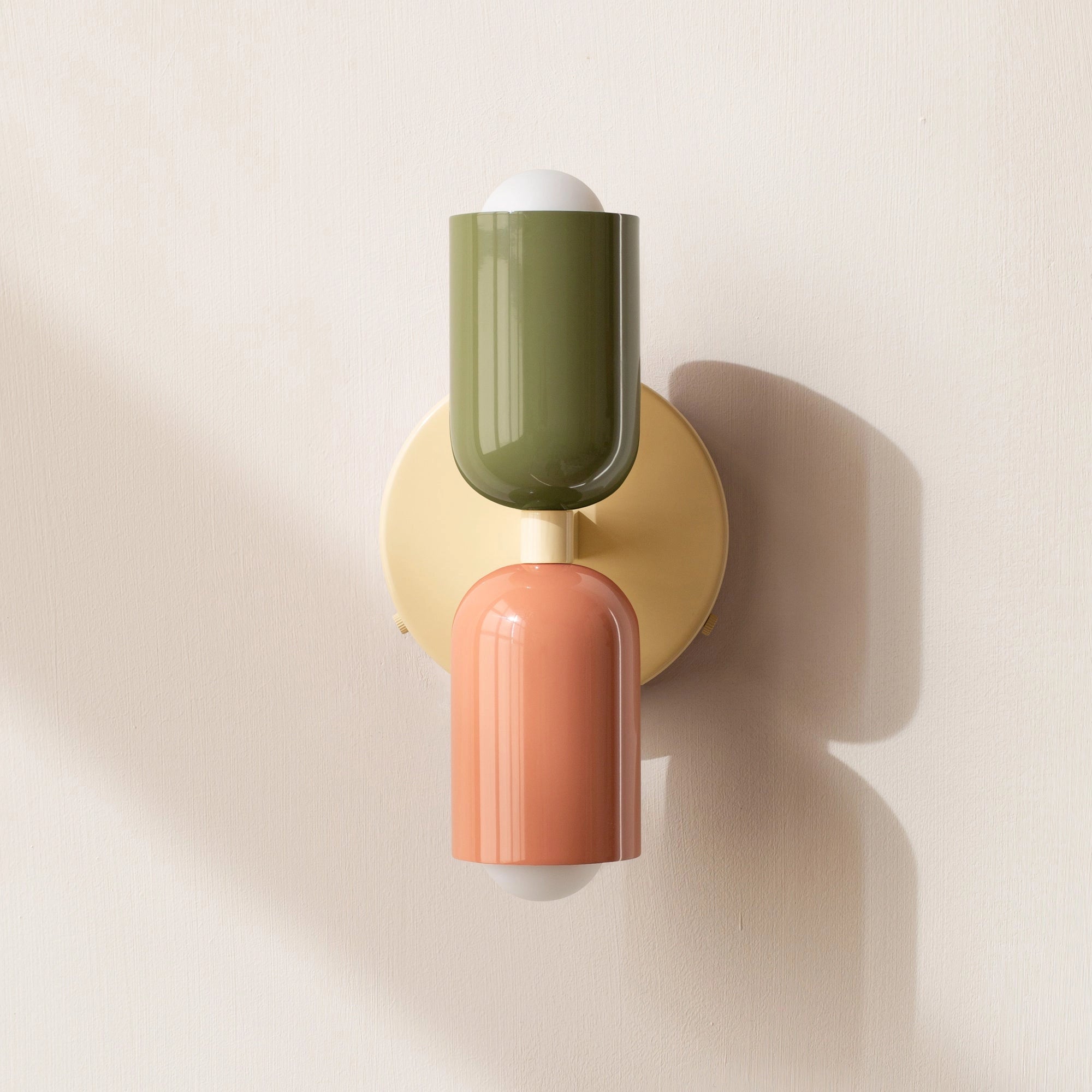 Modern minimalist LED wall sconce with a geometric dual head design, featuring a combination of green, salmon, and beige colors, mounted on a wooden wall.