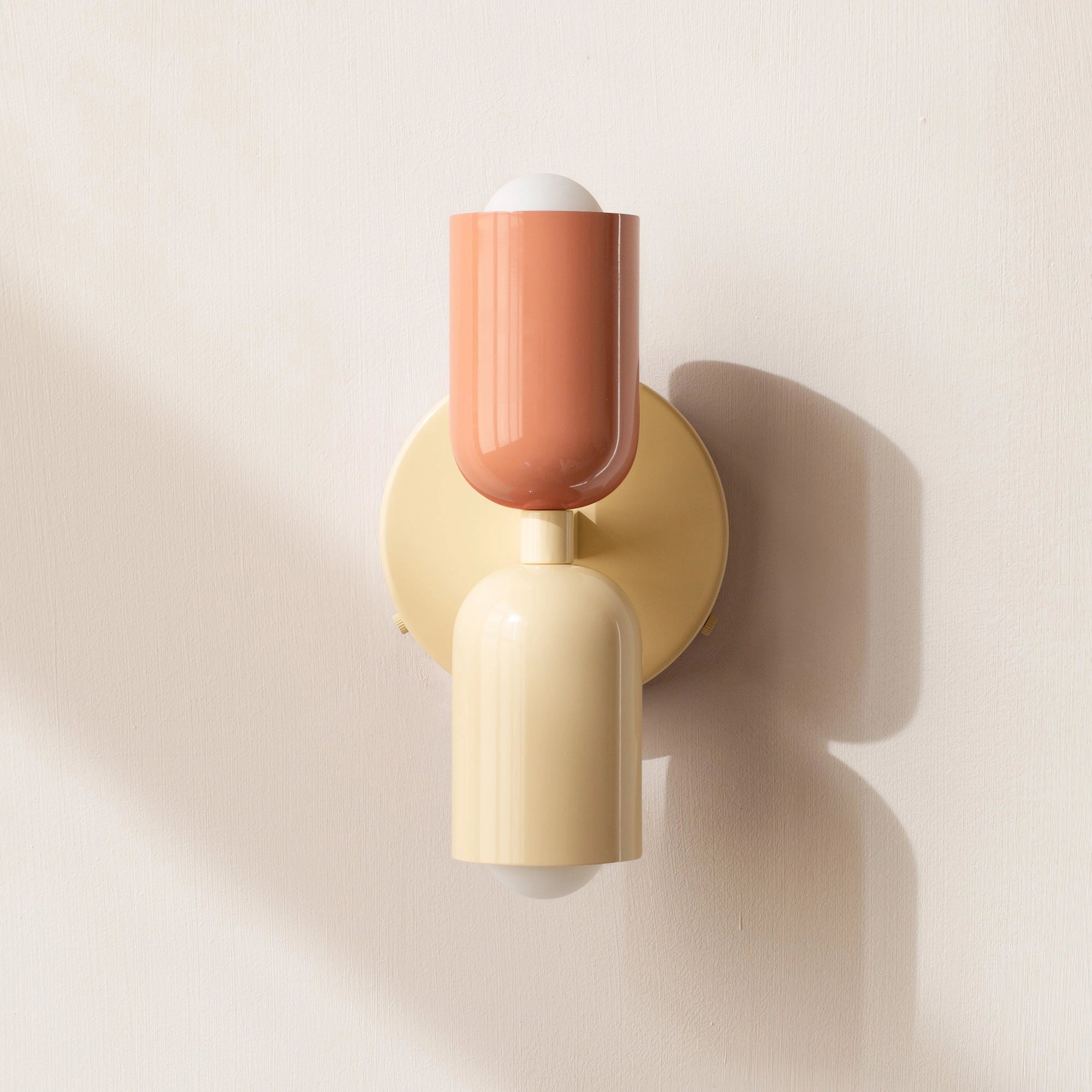 Modern minimalist LED wall sconce with a geometric dual head design, featuring a sleek metal structure in shades of beige and peach, mounted on a wooden base.