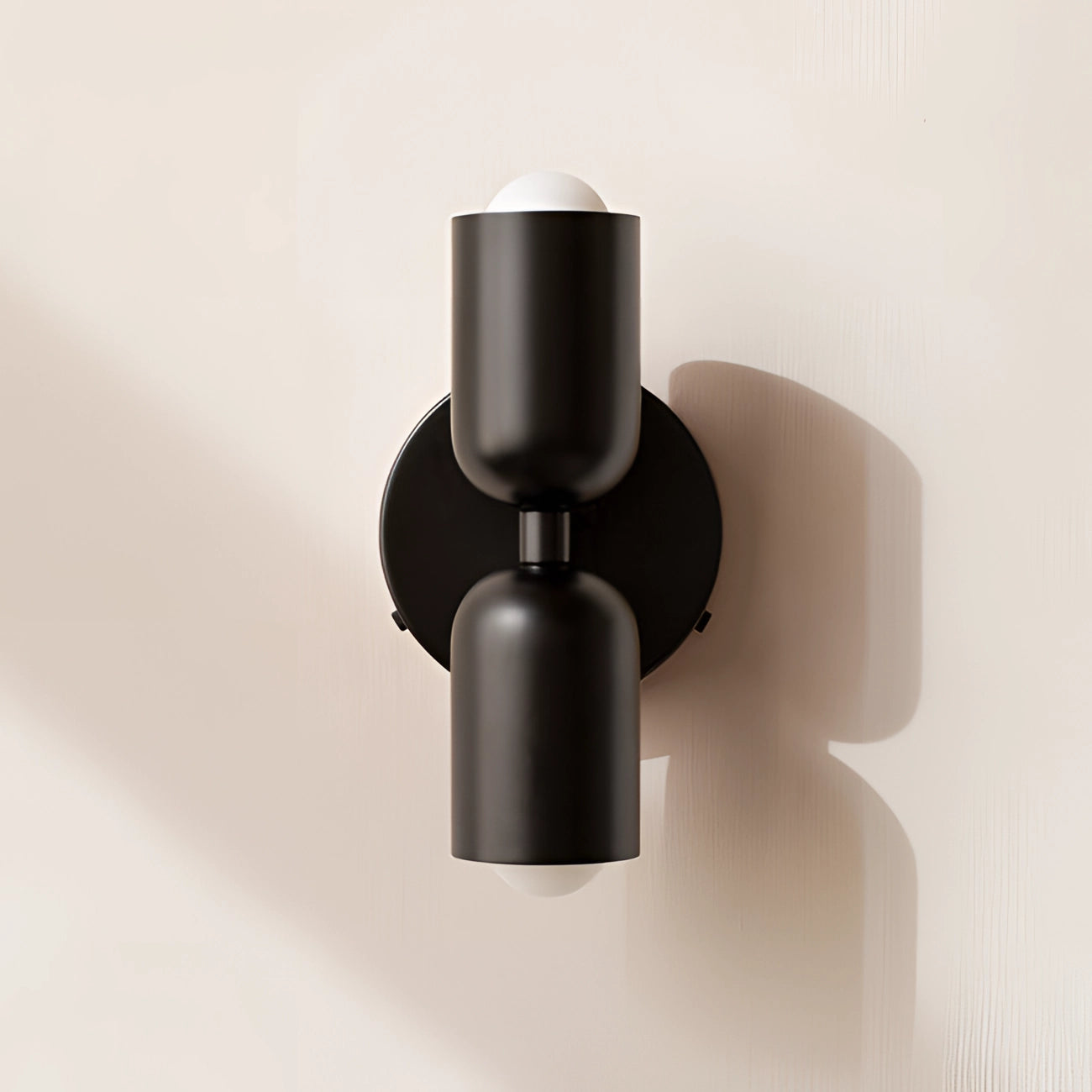A modern minimalist LED wall sconce with a geometric dual head design in black finish, featuring sleek cylindrical elements and a contemporary aesthetic.