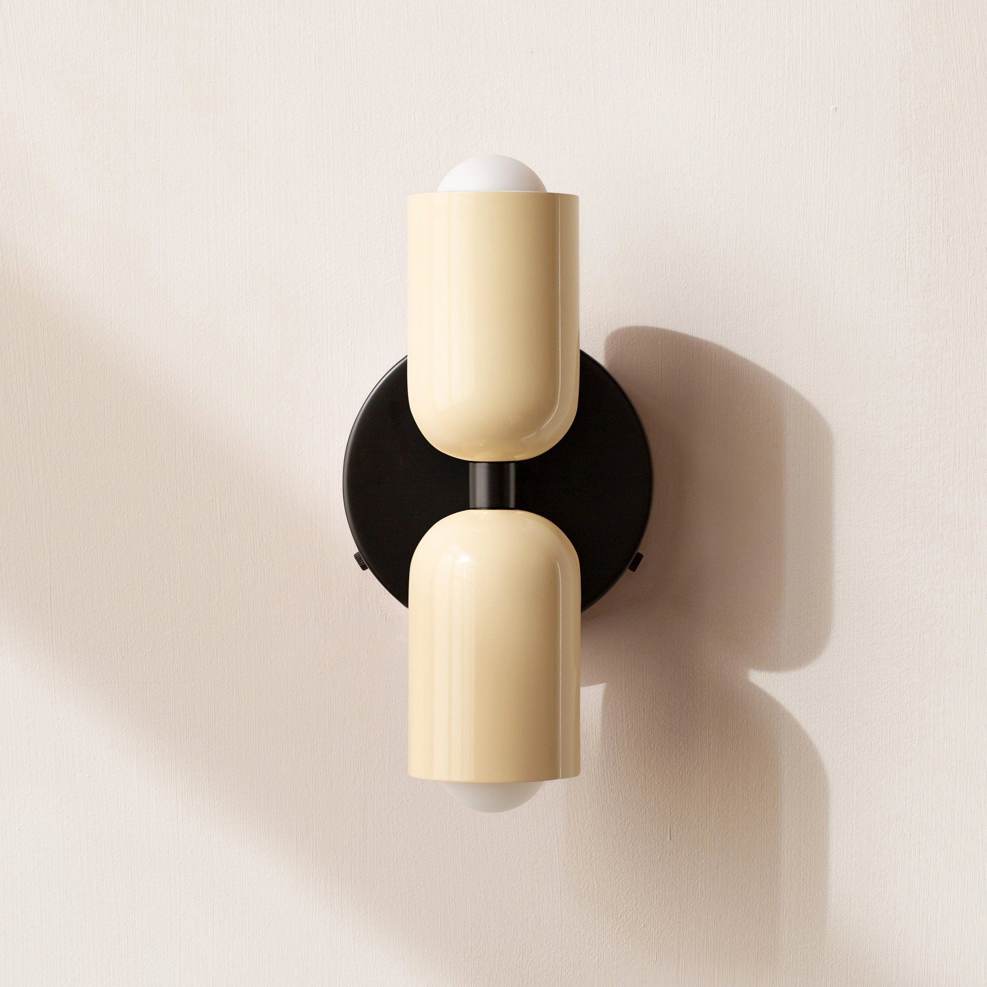 Modern minimalist LED wall sconce with a geometric dual head design, featuring a sleek white and black finish, mounted on a beige wooden background.