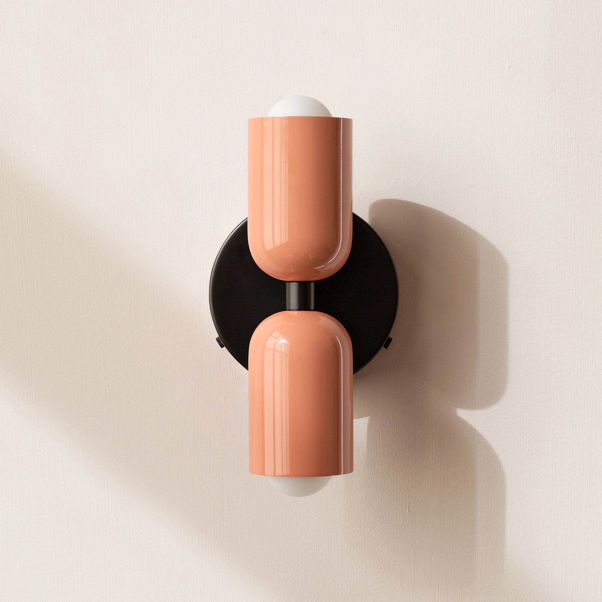 Modern minimalist LED wall sconce with a geometric dual head design in salmon and black color scheme, featuring sleek cylindrical shapes and contemporary style.