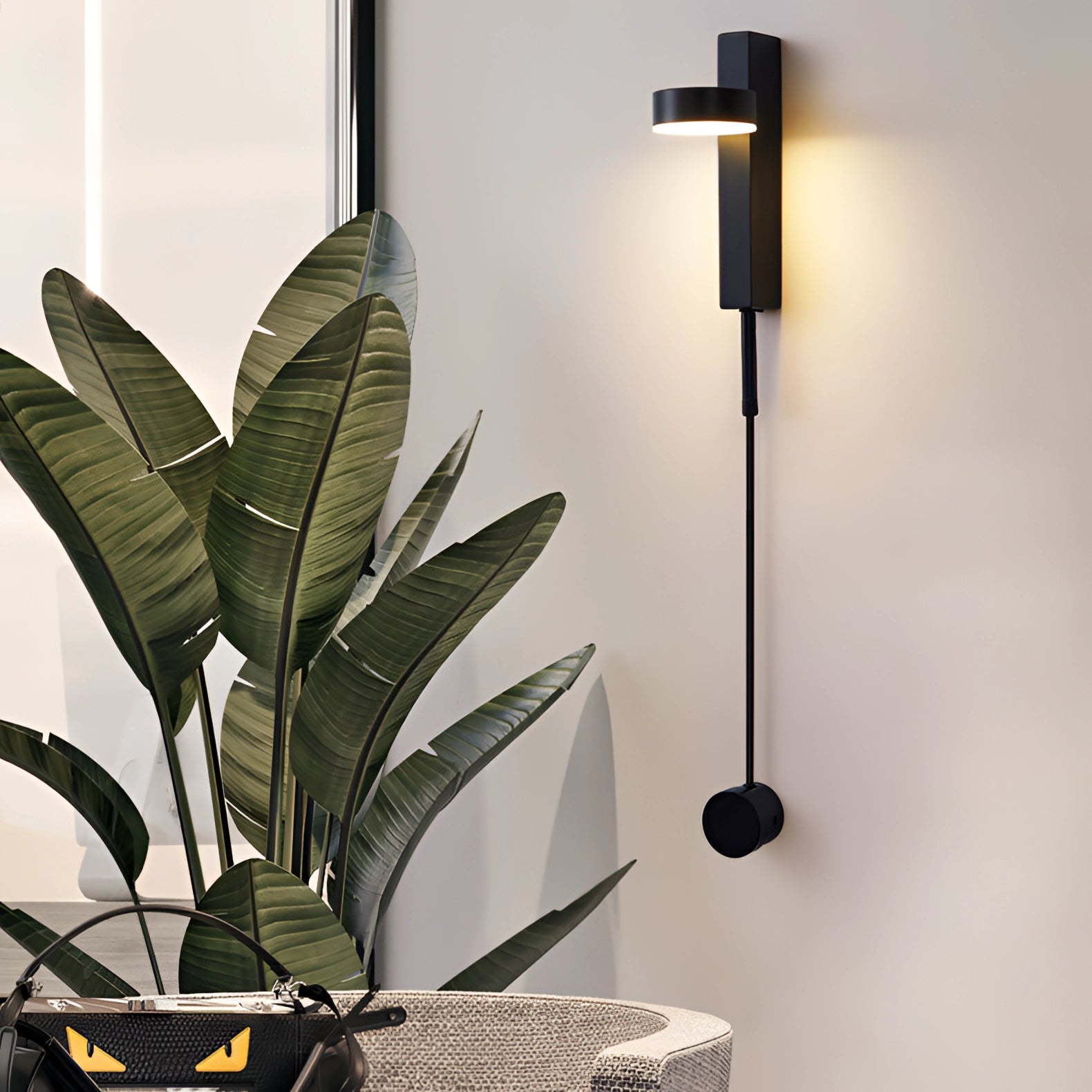 Modern minimalist black LED wall sconce installed on a white wall in a bedroom, featuring an adjustable fixture emitting white light (5000K), complemented by indoor plants and decor elements.