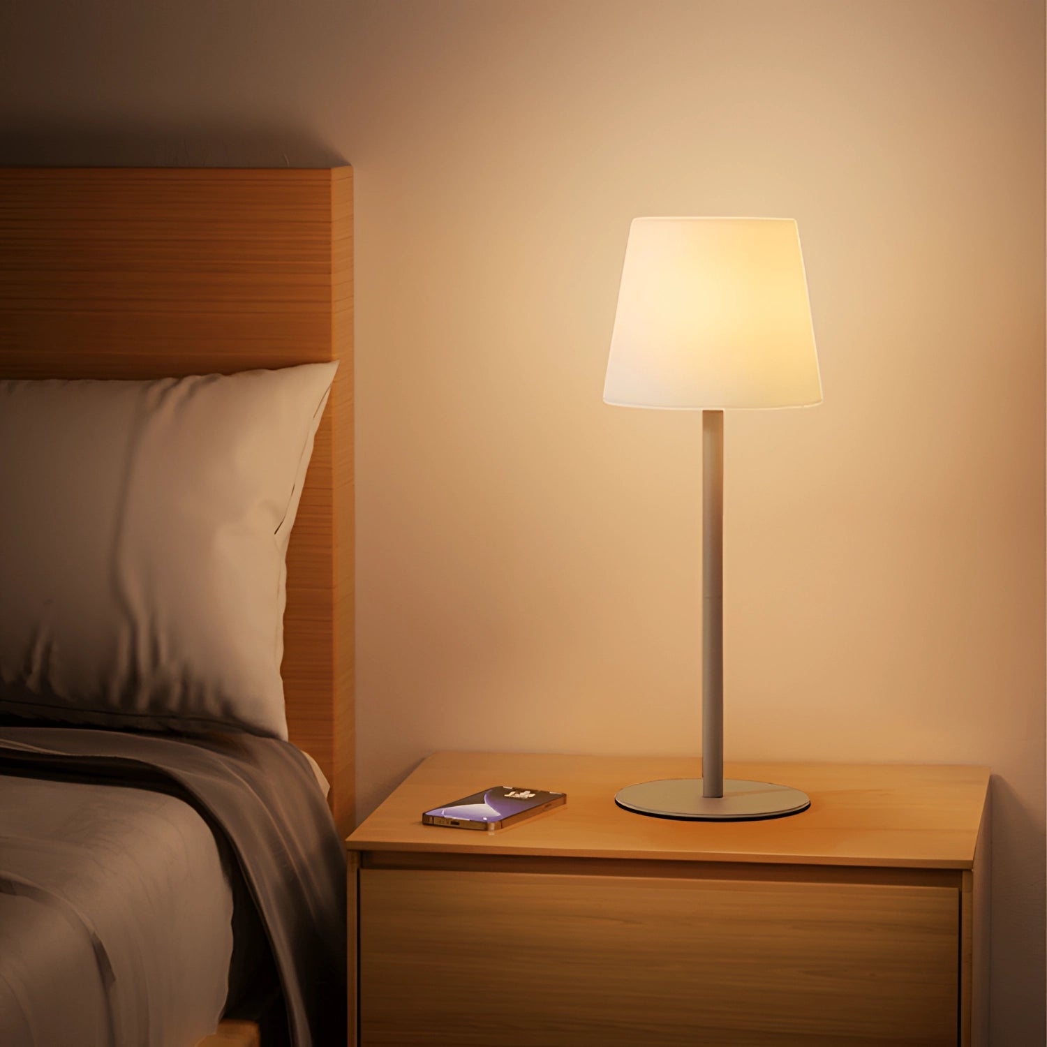 Modern minimalist pastel table lamp with a wooden base, situated in a chic interior setting with hardwood flooring and a neutral-toned wall, enhancing the comfort and style of the living room or bedroom decor.