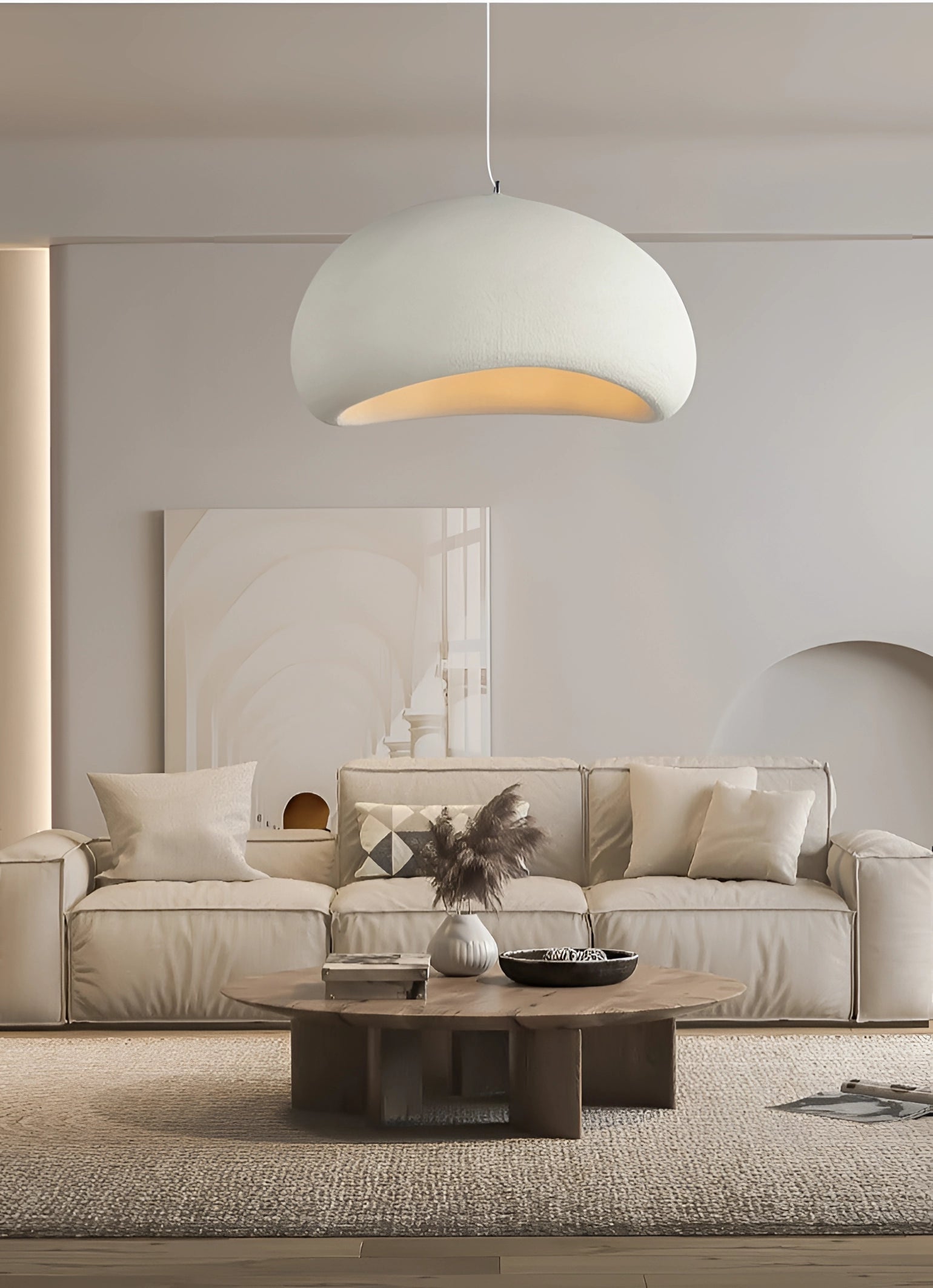 Modern minimalist pendant lights with a Scandinavian design hanging above a kitchen area, enhancing the interior with sleek and contemporary lighting. The image features a cozy living space with a couch and table in a neutral, grey color palette, emphasizing a clean and comfortable aesthetic.