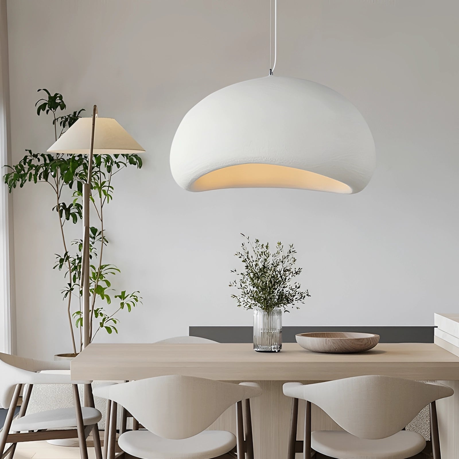 Modern minimalist pendant lights hanging above a Scandinavian-style kitchen with a white table, chairs, and green plant accents.