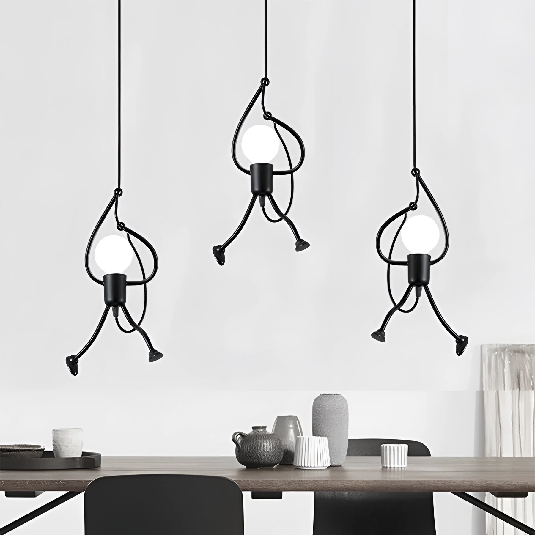 A modern minimalist pendant light with a unique sculptural design hanging above a table in a black-and-white interior setting.