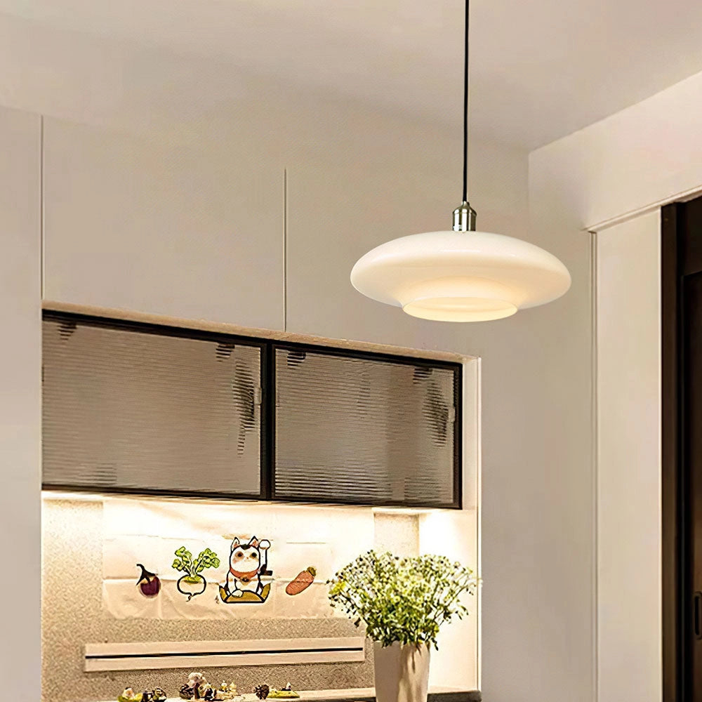 A modern minimalist pendant light with frosted glass and adjustable height, hanging in an interior room with houseplants and a flowerpot near a window.