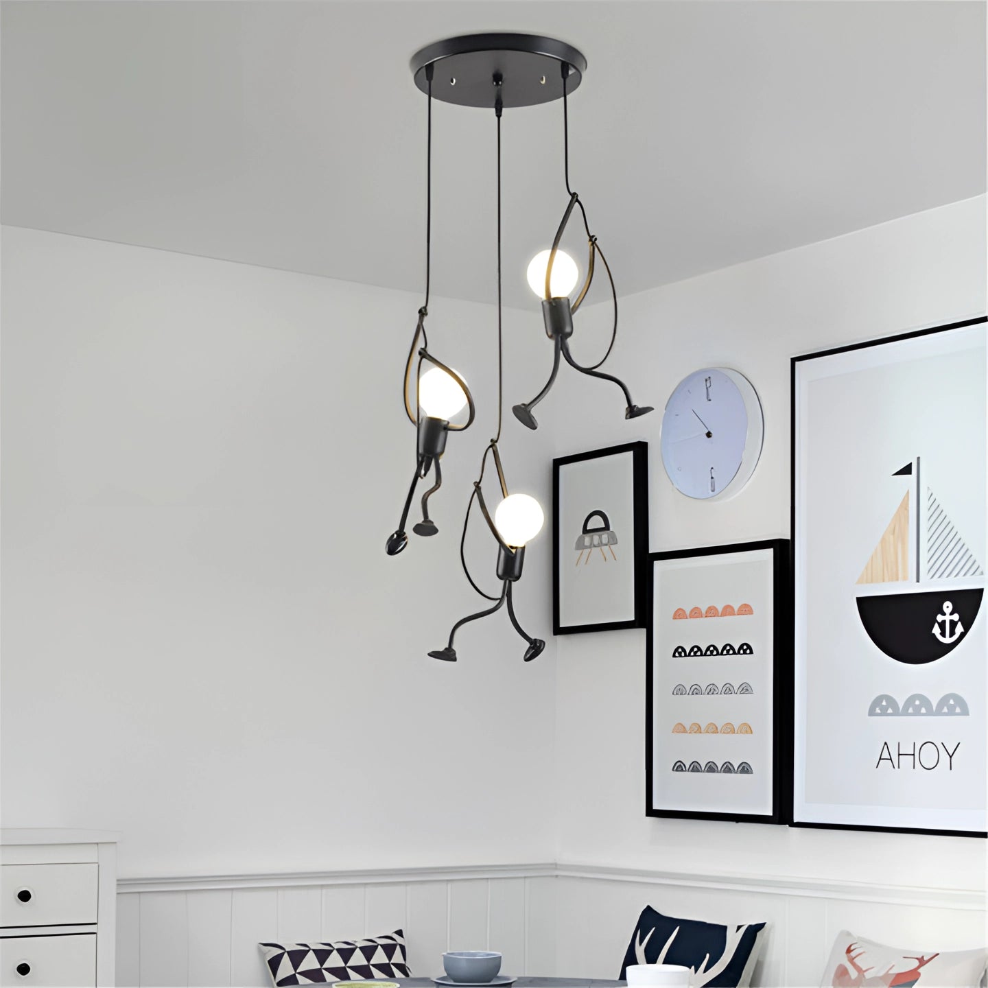Modern minimalist pendant light with three sculptural lamps arranged in a circle, hanging from the ceiling in a white interior-designed room with wall art and a clock.
