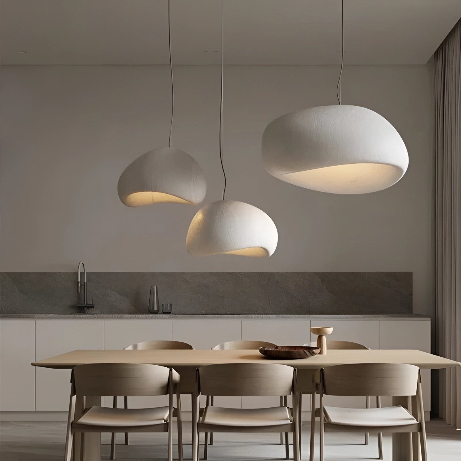 Modern minimalist pendant lights hanging above a wooden dining table with chairs, showcasing Scandinavian kitchen interior design elements, featuring sleek furniture and wood flooring.