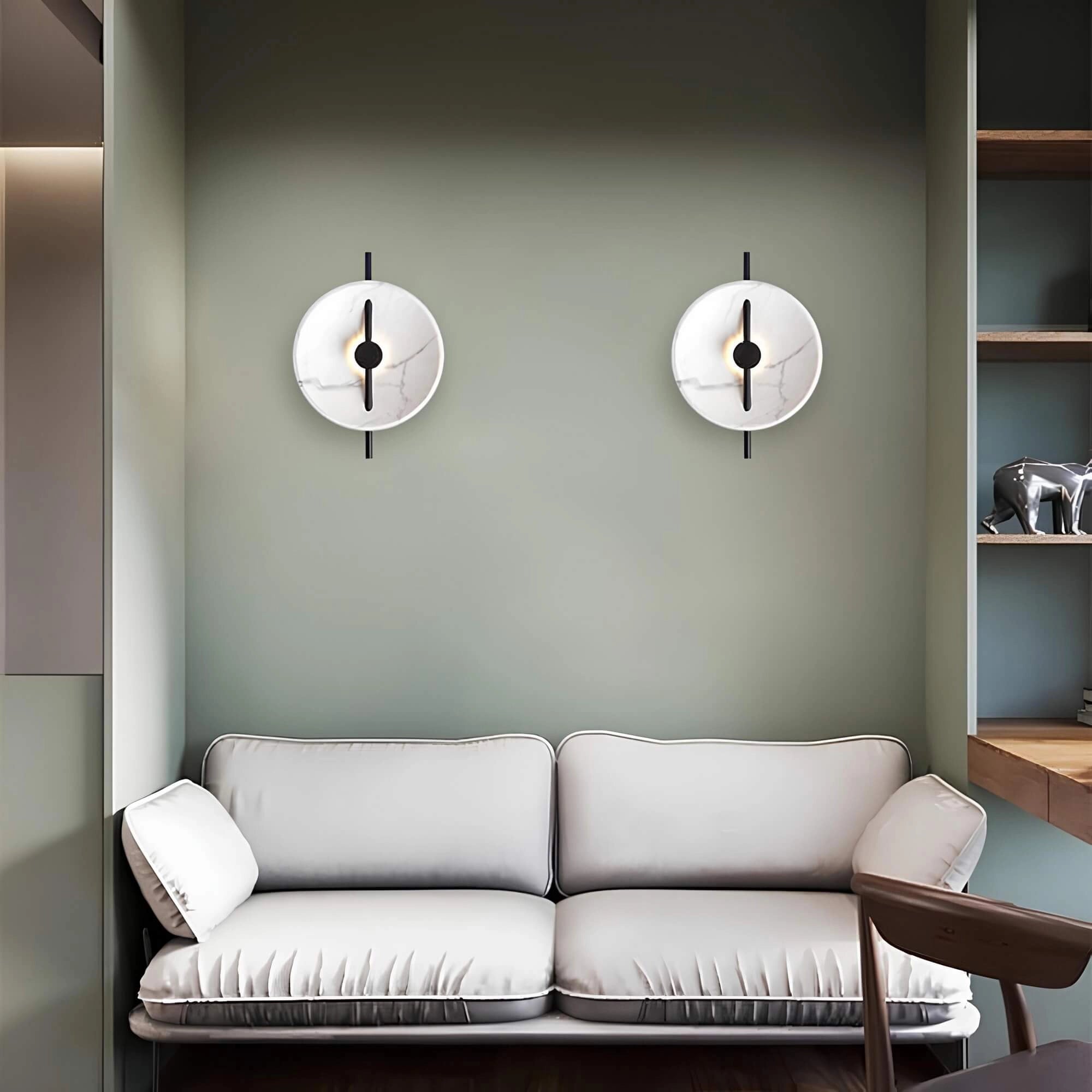 Modern minimalist silver round wall clock hanging on a wall in a stylish living room with brown and grey furniture, including a couch, and contemporary interior design elements.