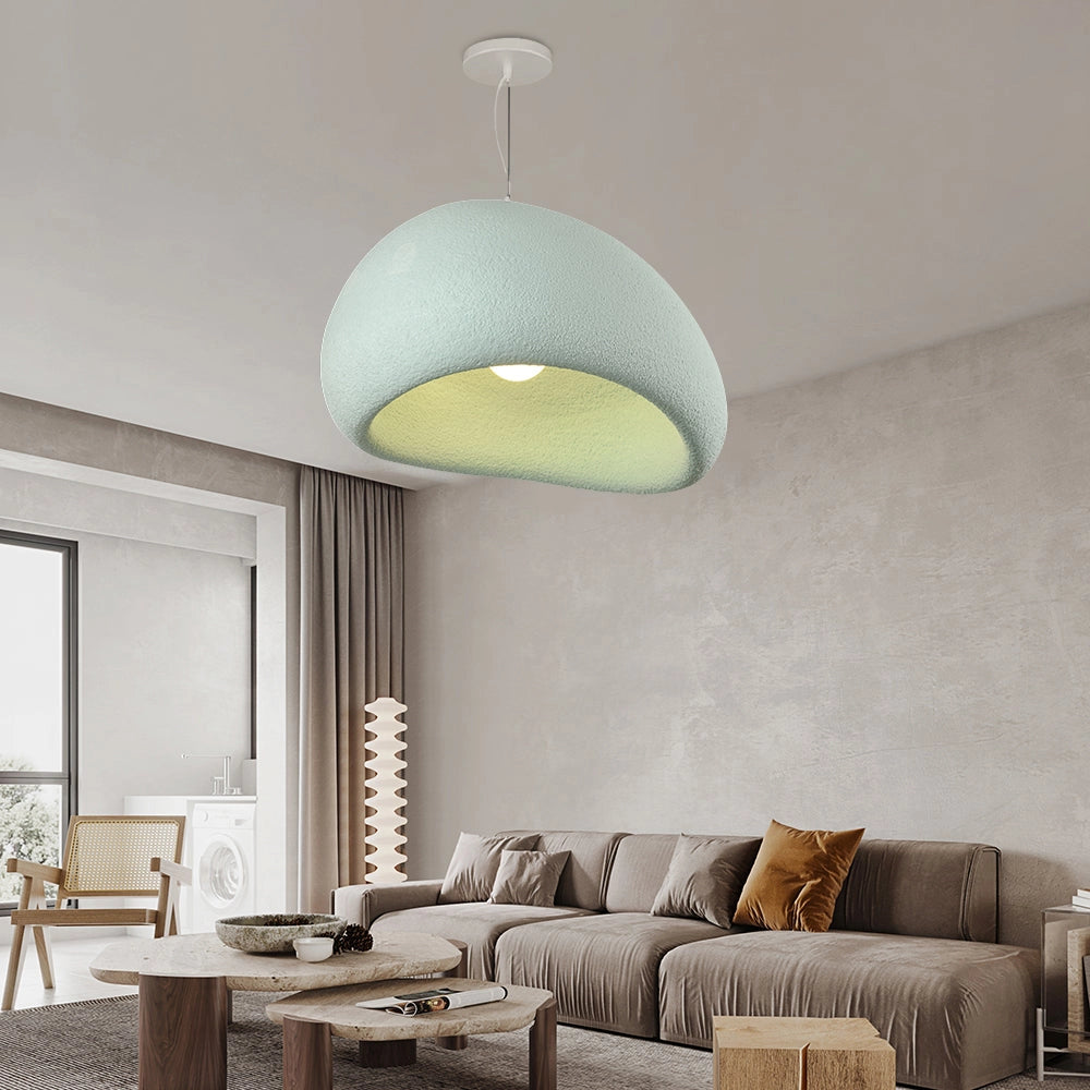 Modern minimalist white dome pendant light hanging above a blue table in an elegantly decorated living room with a beige couch, wooden accents, and picture frames on the walls.