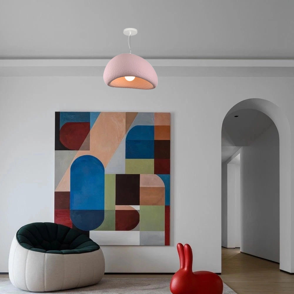 Modern minimalist white dome pendant light in a pink hue, elegantly suspended from the ceiling, enhancing the interior design of a stylish room with wooden flooring and artistic decor elements.