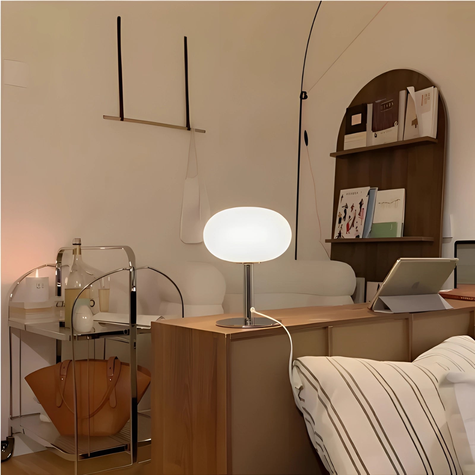 A modern minimalist white globe table lamp with a sleek chrome base, placed on a wooden surface in a well-lit living room setting.