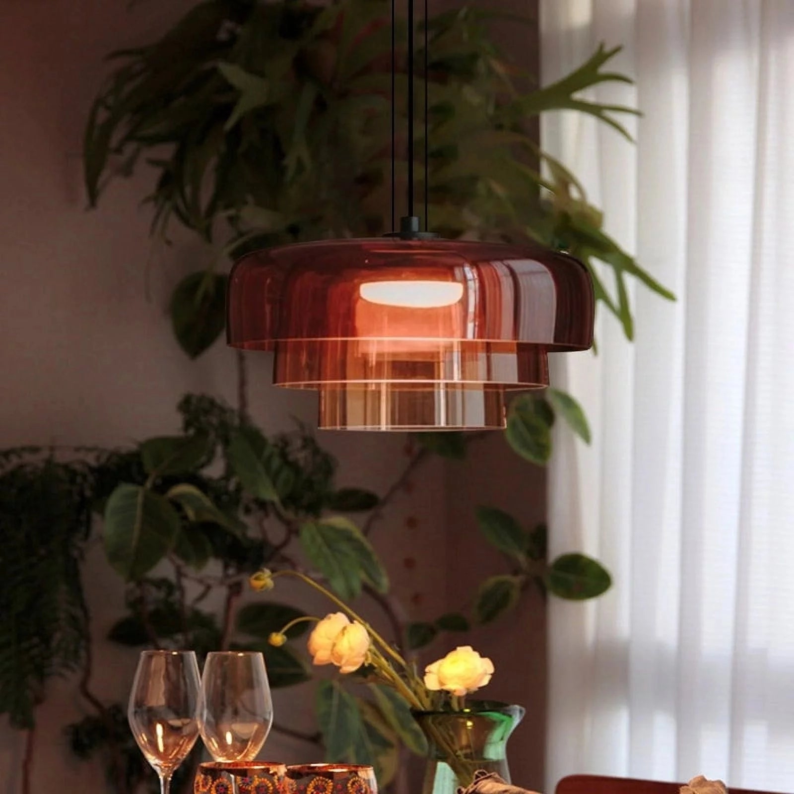 Modern multi-colored glass pendant light hanging above a wooden table set with tableware, wine glasses, and a flowerpot, with houseplants in the background, showcasing contemporary interior design.