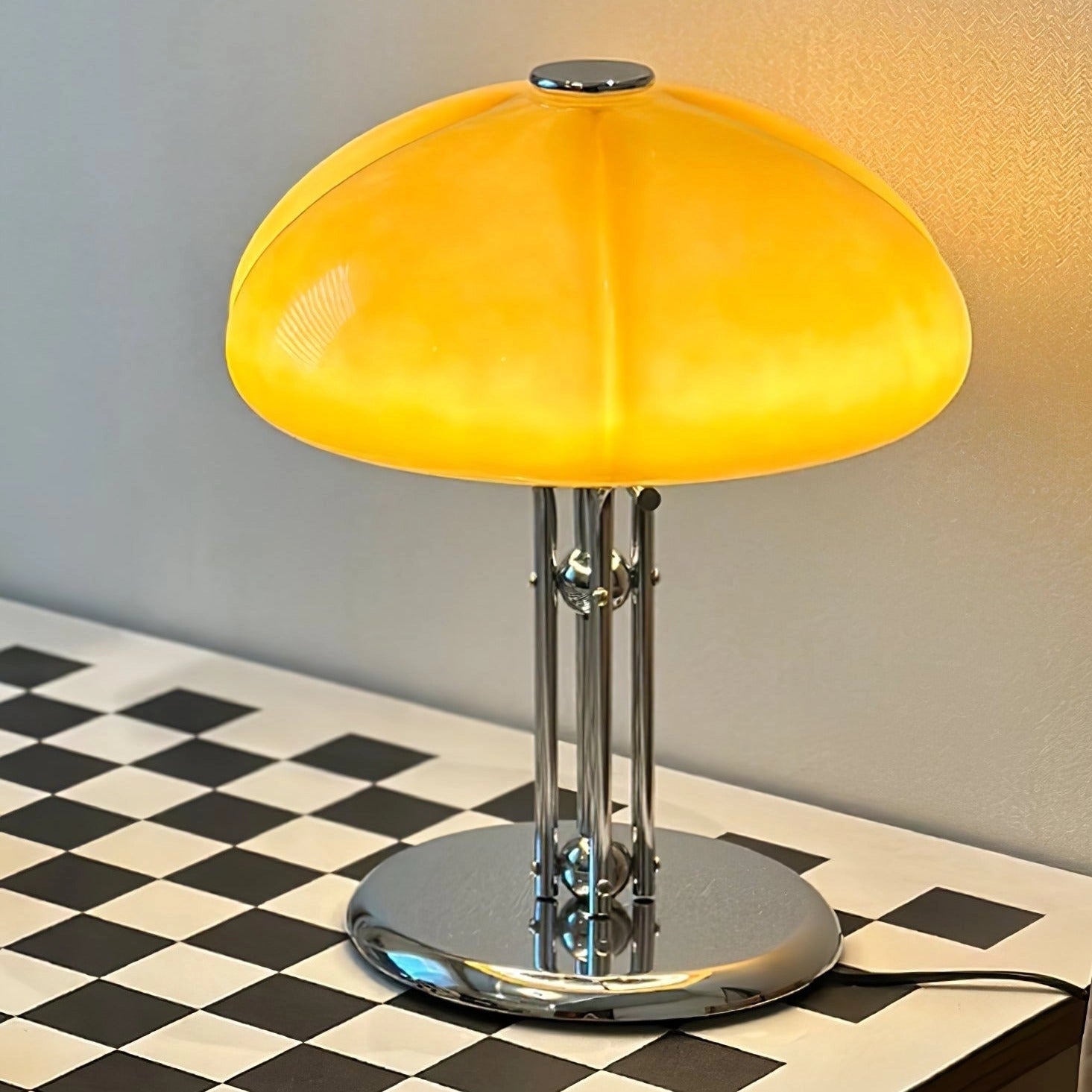 Modern orange globe table lamp with chrome base providing warm light, positioned on a table near a chair and shelf, featuring decorative art elements.