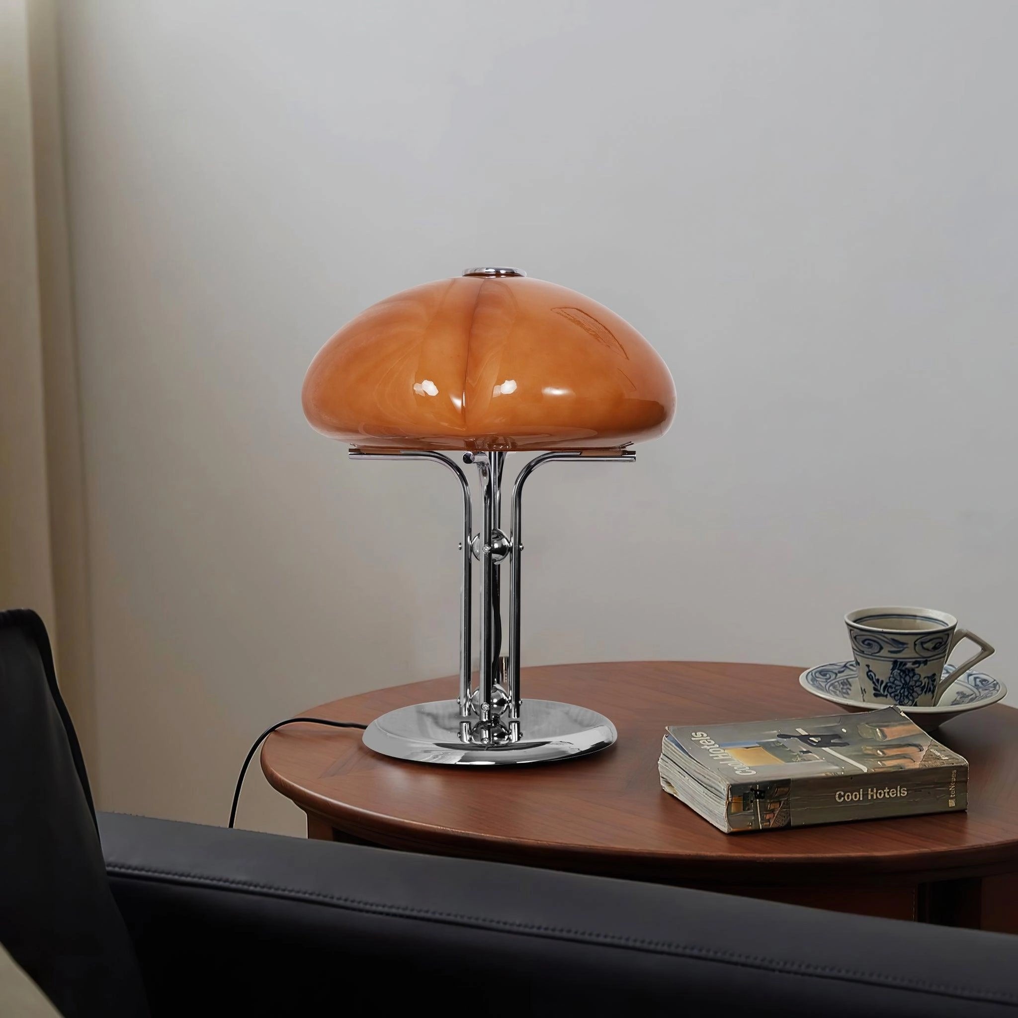 Modern orange globe table lamp with chrome base and warm light on a wooden table with shelving in the background.
