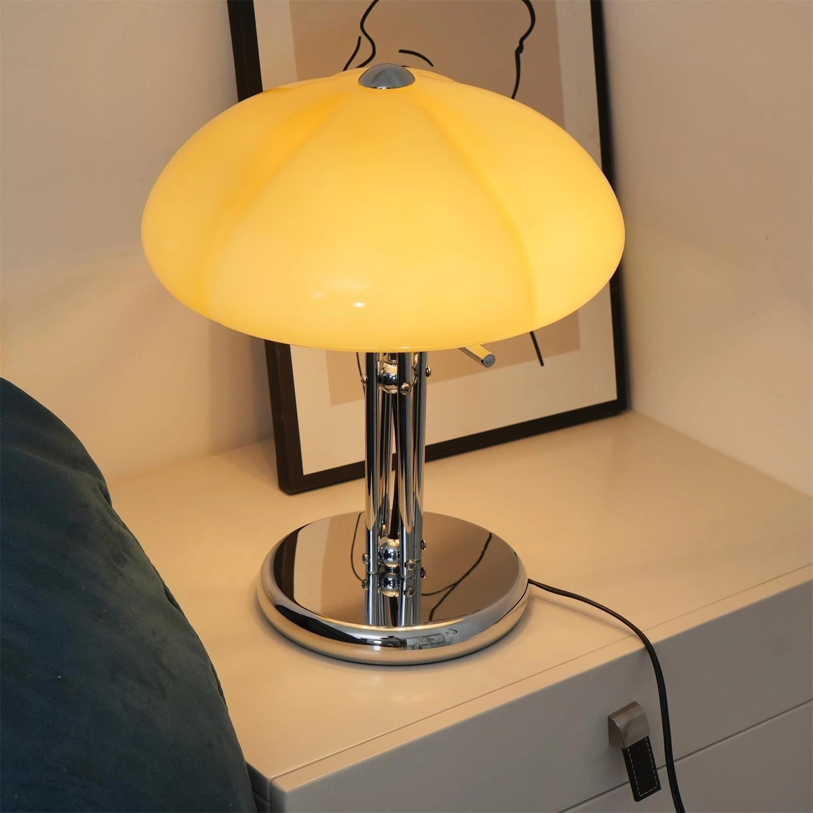 Modern orange globe table lamp with chrome base emitting warm light, placed on a wooden table in a well-designed room interior.