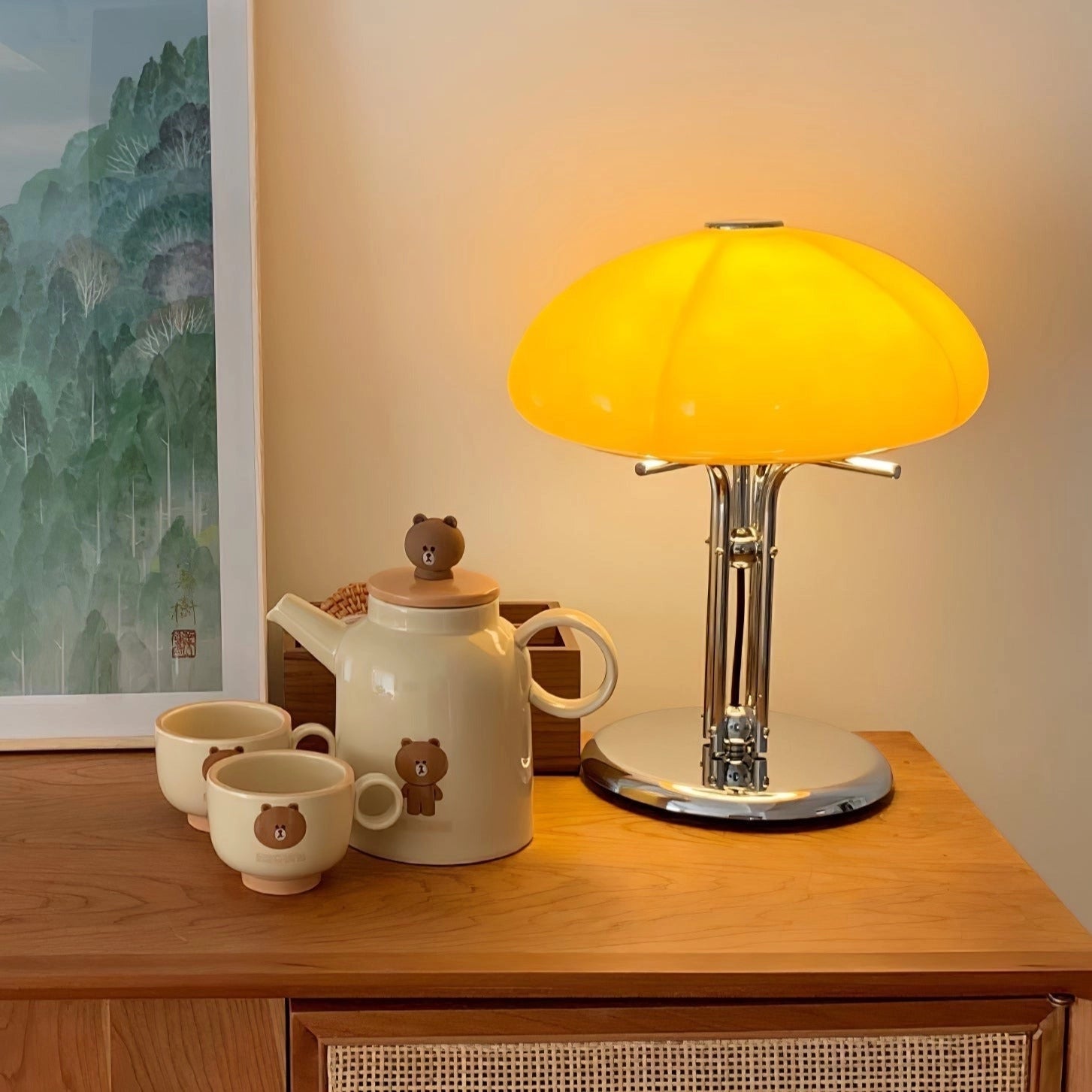 Modern orange globe table lamp with a chrome base emitting warm light, placed on a wooden table next to a coffee cup and dishware.