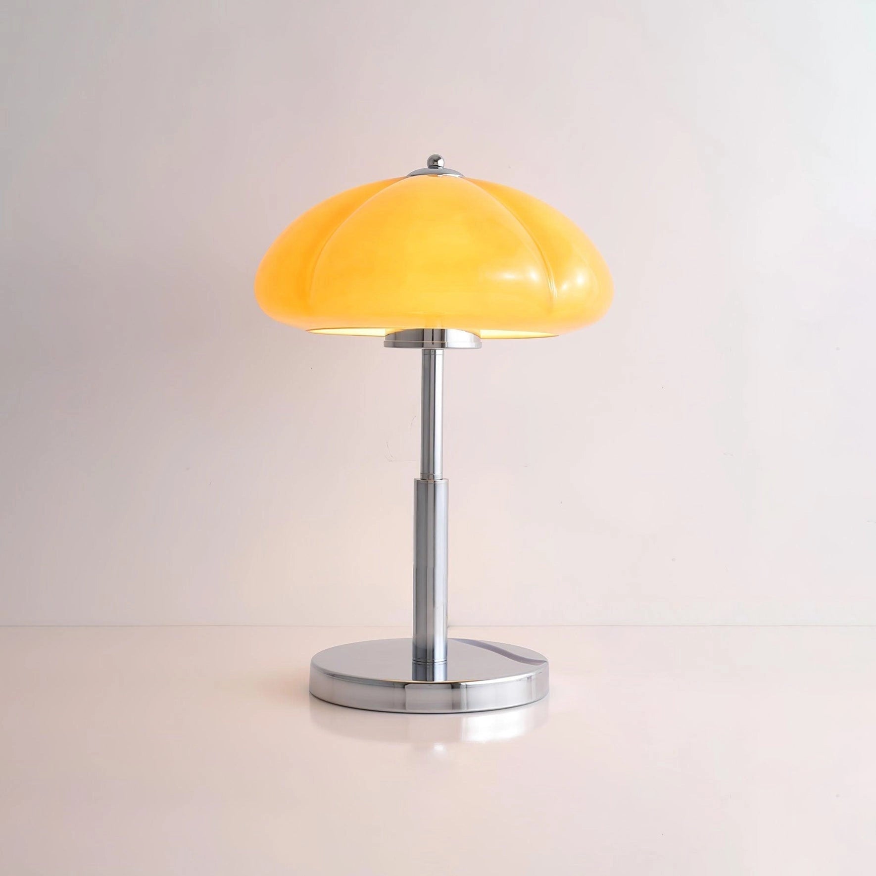Modern orange globe table lamp with chrome base and warm light, placed on a wooden table near a plant.