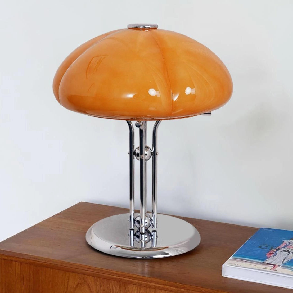Modern orange globe table lamp with chrome base, emitting warm light, placed on a wooden table.