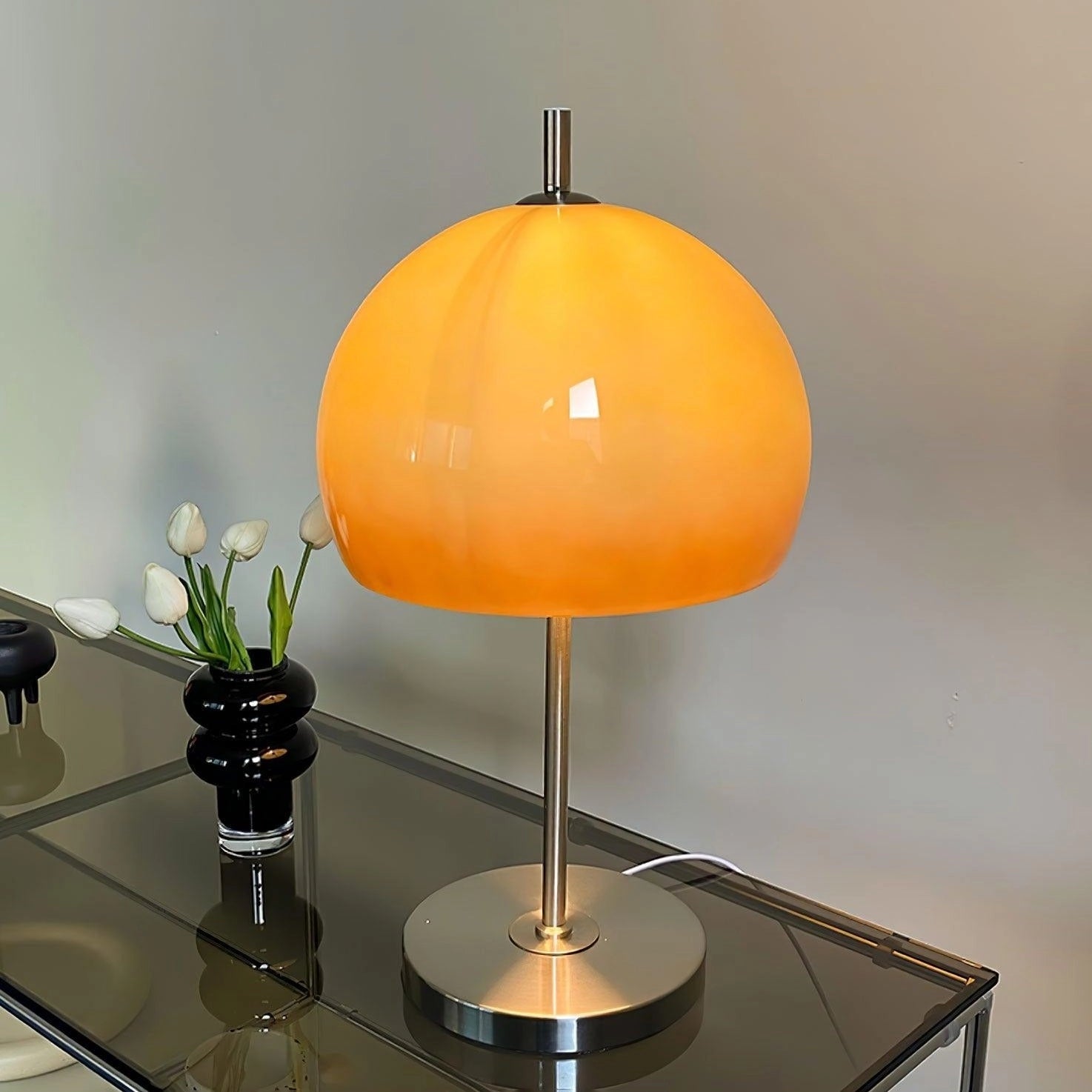Modern orange globe table lamp with chrome base and warm light, styled on a table next to a flowerpot with a plant, decorative accent piece.