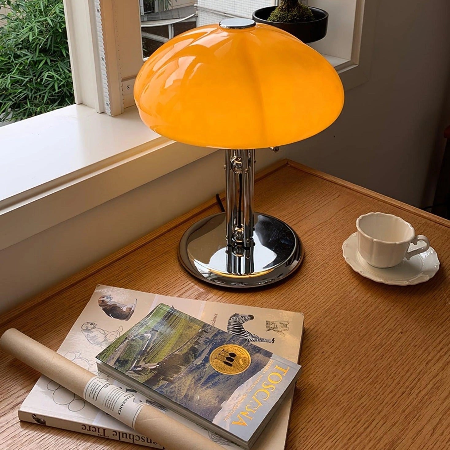 Modern orange globe table lamp with chrome base emitting warm light on a wooden table.