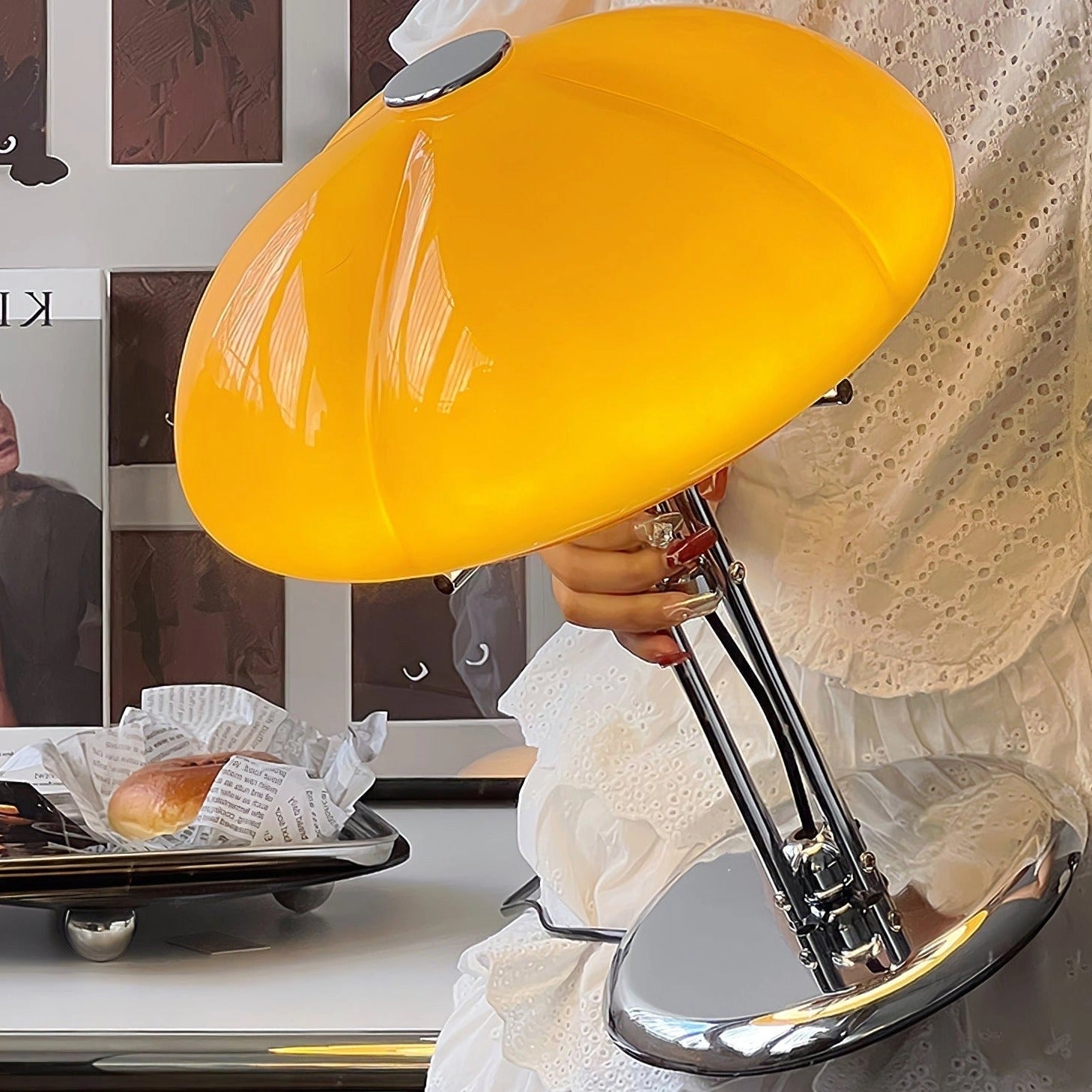 Modern orange globe table lamp with chrome base, emitting warm light, placed on a table next to a chair.