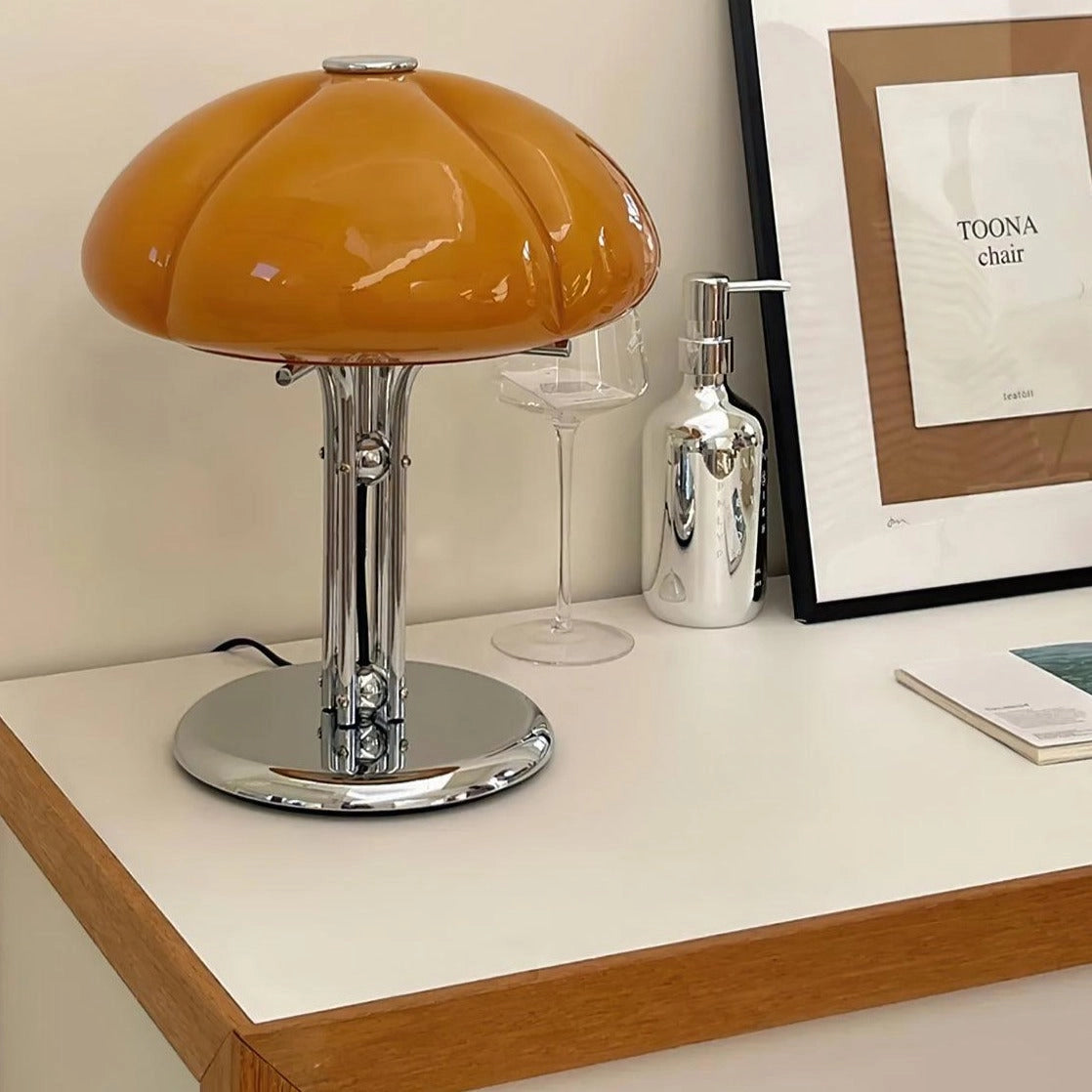Modern orange globe table lamp with chrome base and warm light, placed on a wooden table in a room.