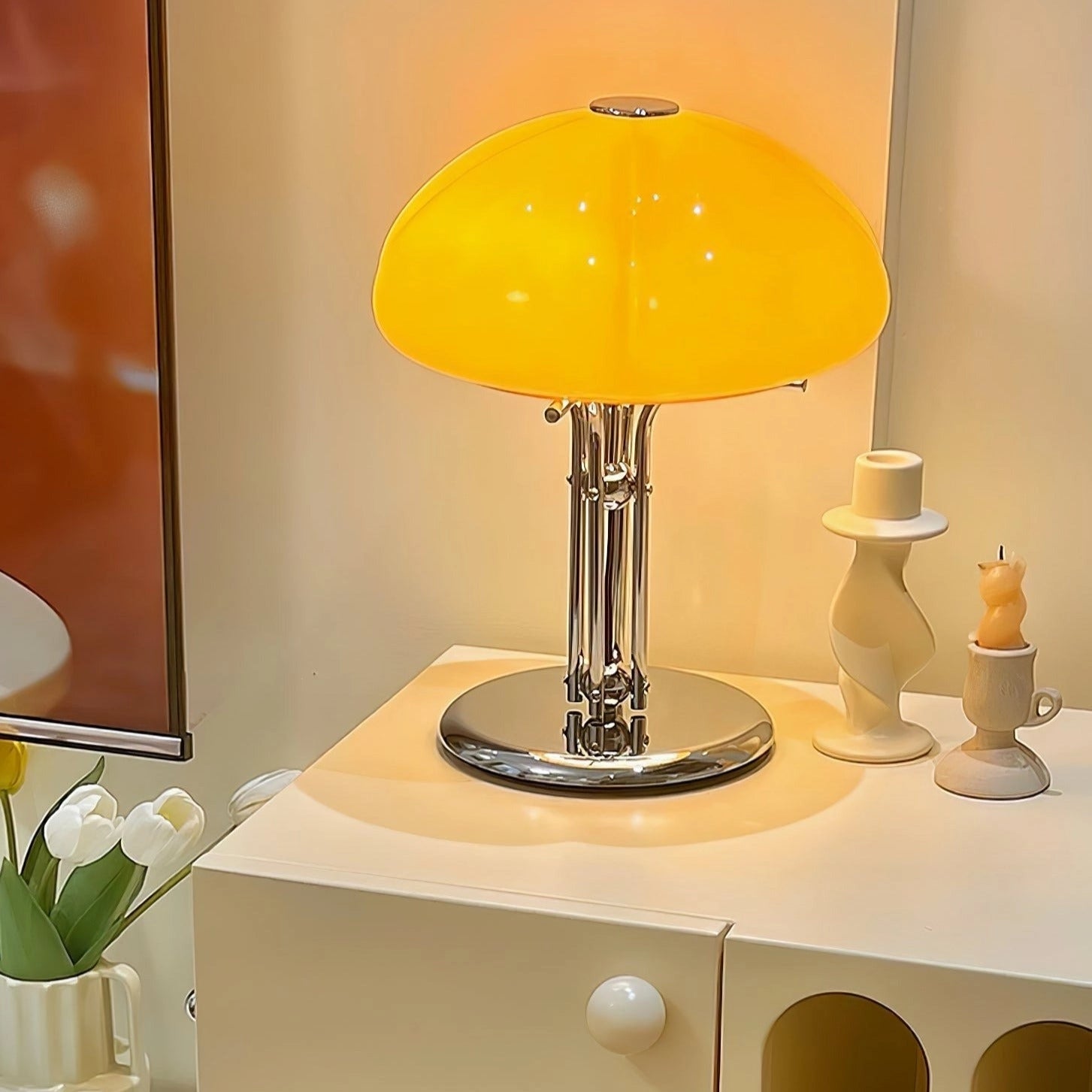 Modern orange globe table lamp with chrome base and warm light, placed on a table in an interior setting.