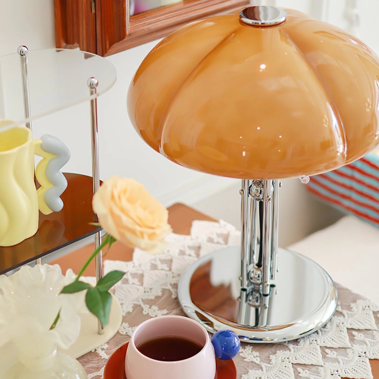 Modern orange globe table lamp with chrome base emitting warm light, placed on a table next to a coffee cup and saucer.